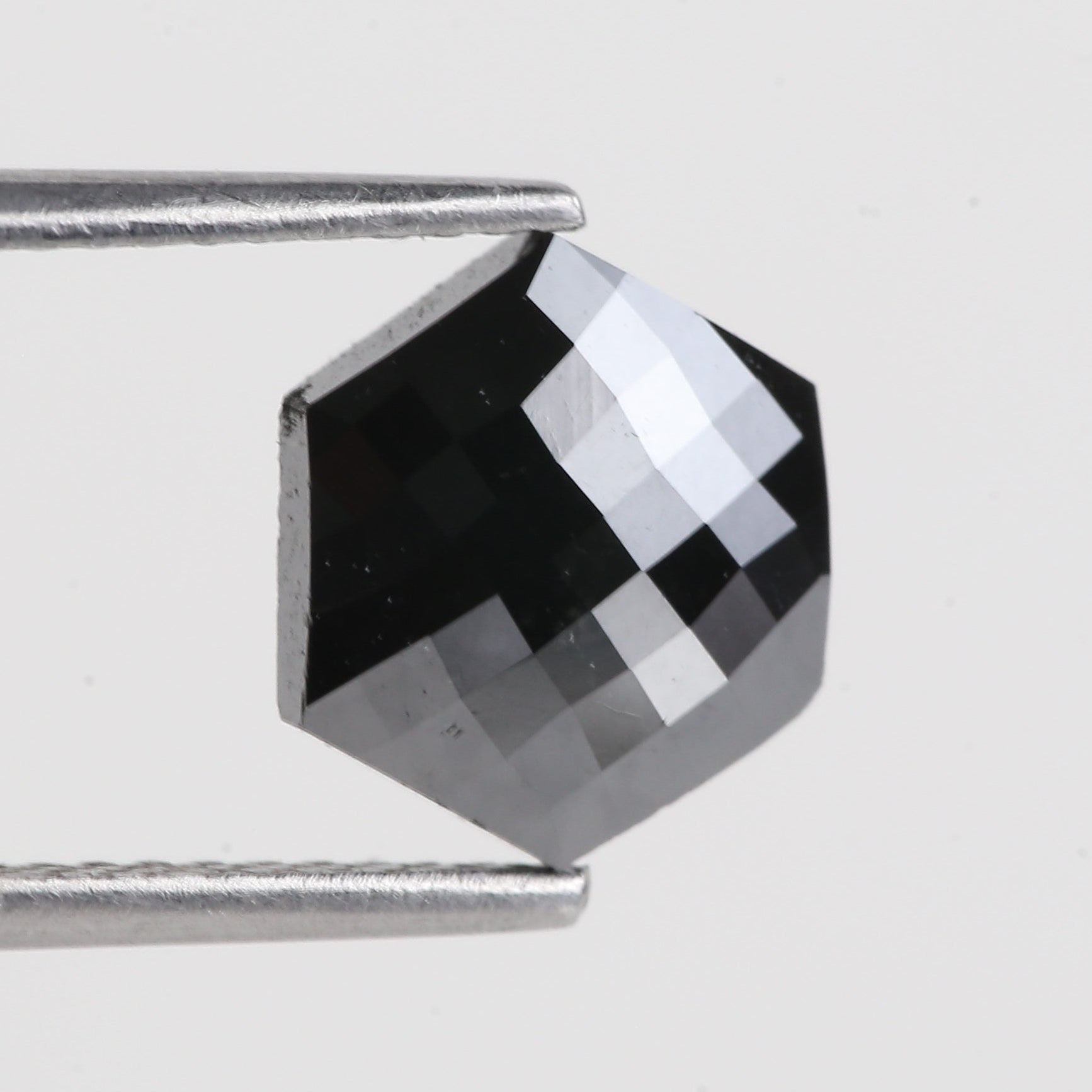 Faceted gemstone held by tweezers on a light gray background