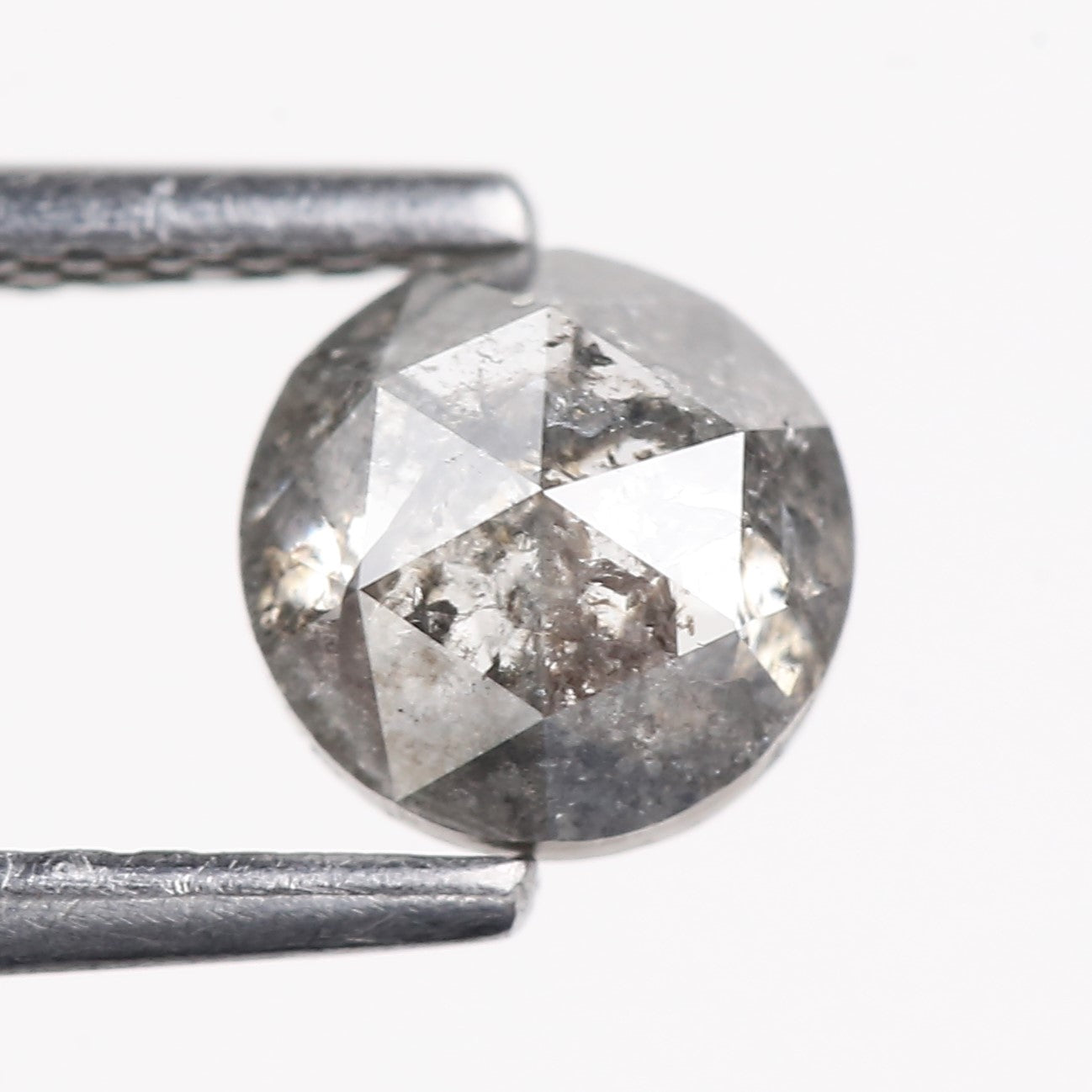 Raw diamond held between two metal prongs on a white background