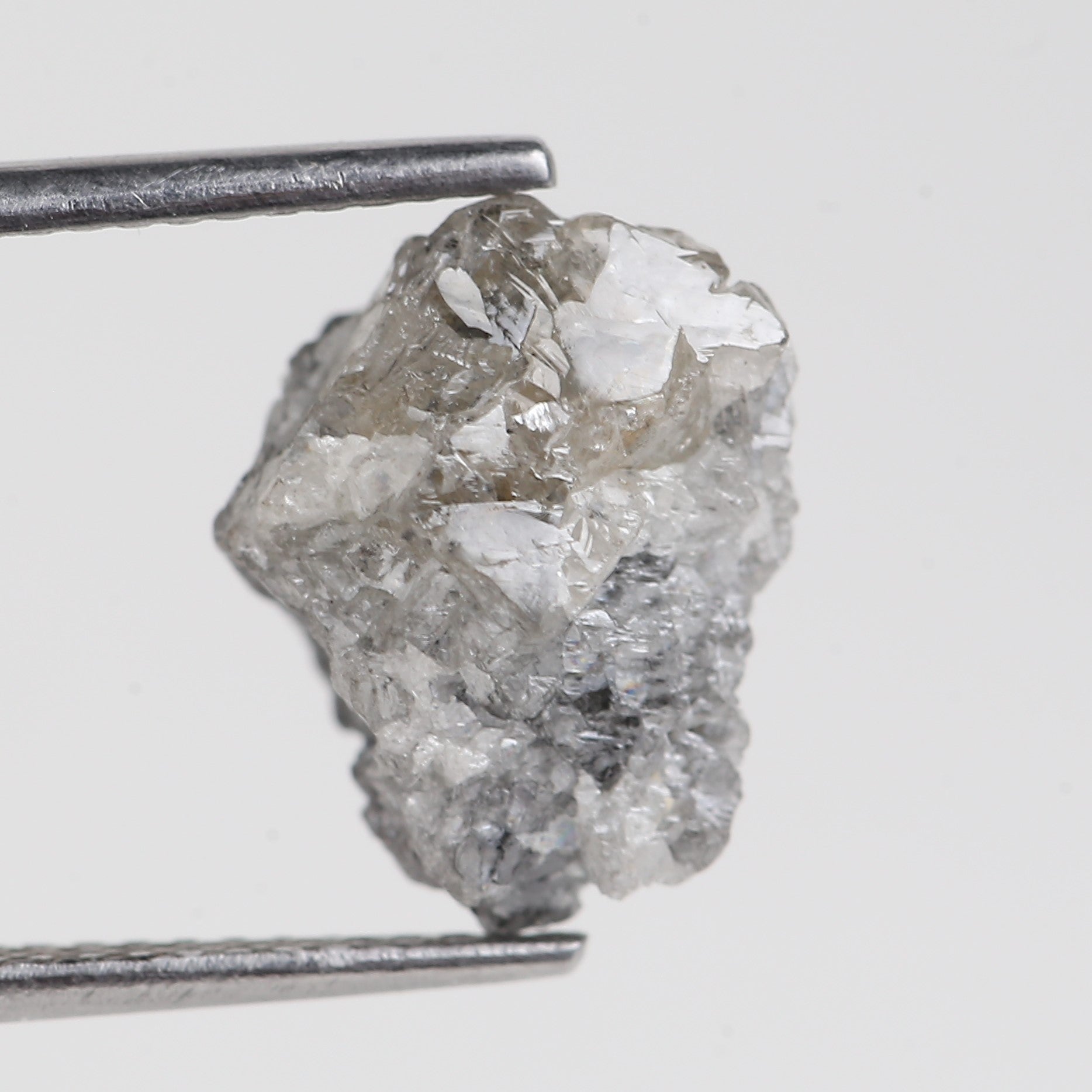 Raw diamond crystal held by tweezers on a light gray background