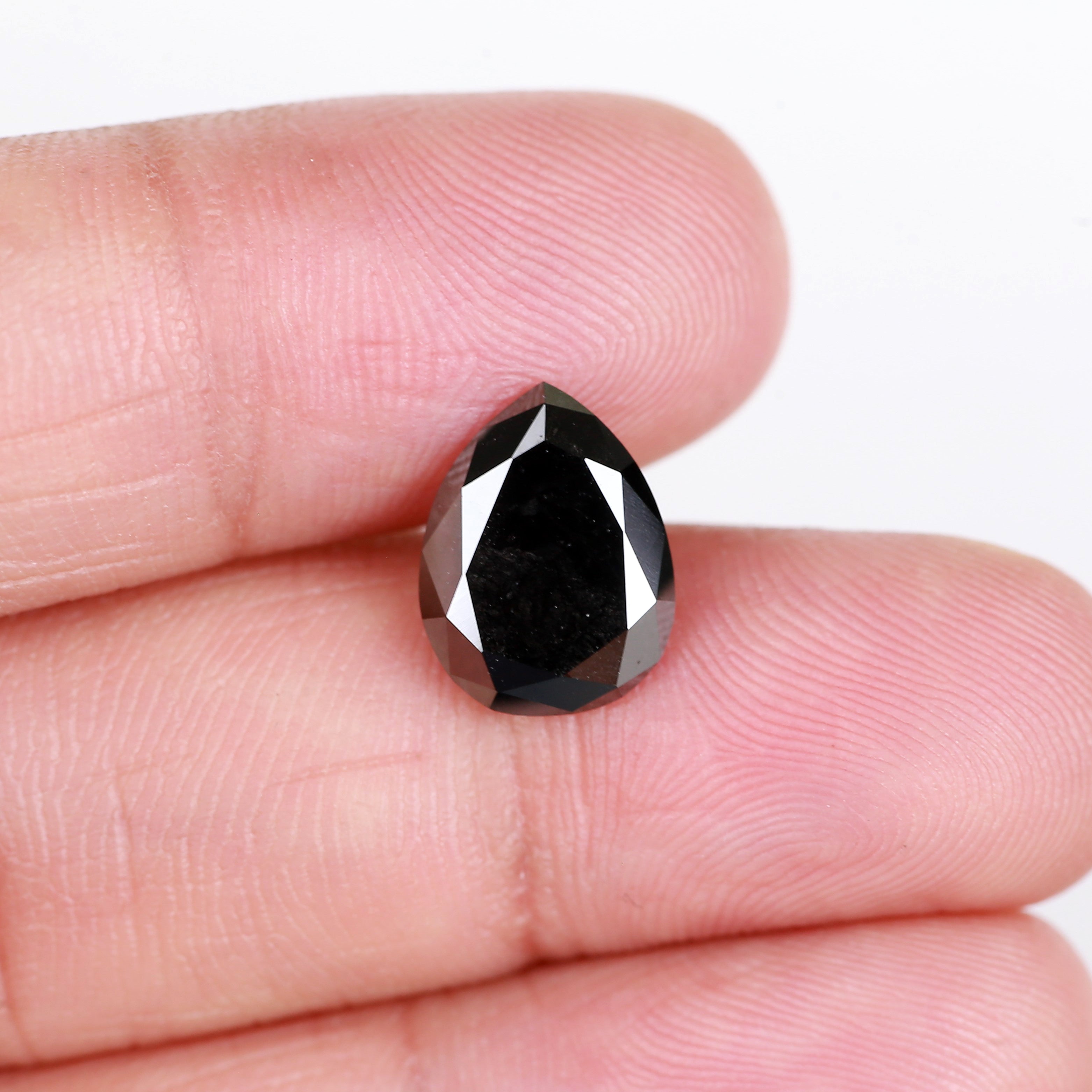 Black teardrop-shaped gemstone held between two fingers on a white background
