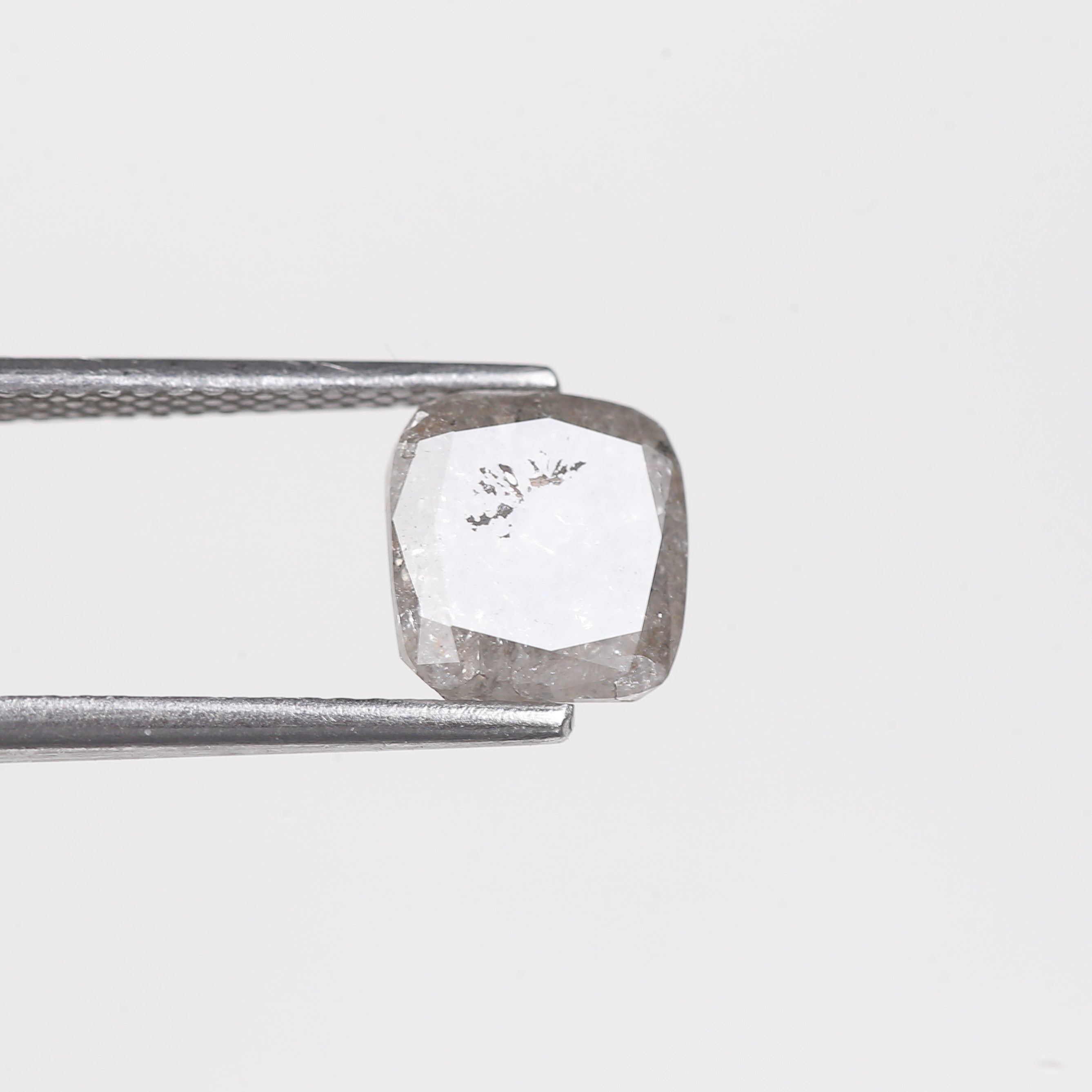 Raw diamond held by tweezers on a light gray background