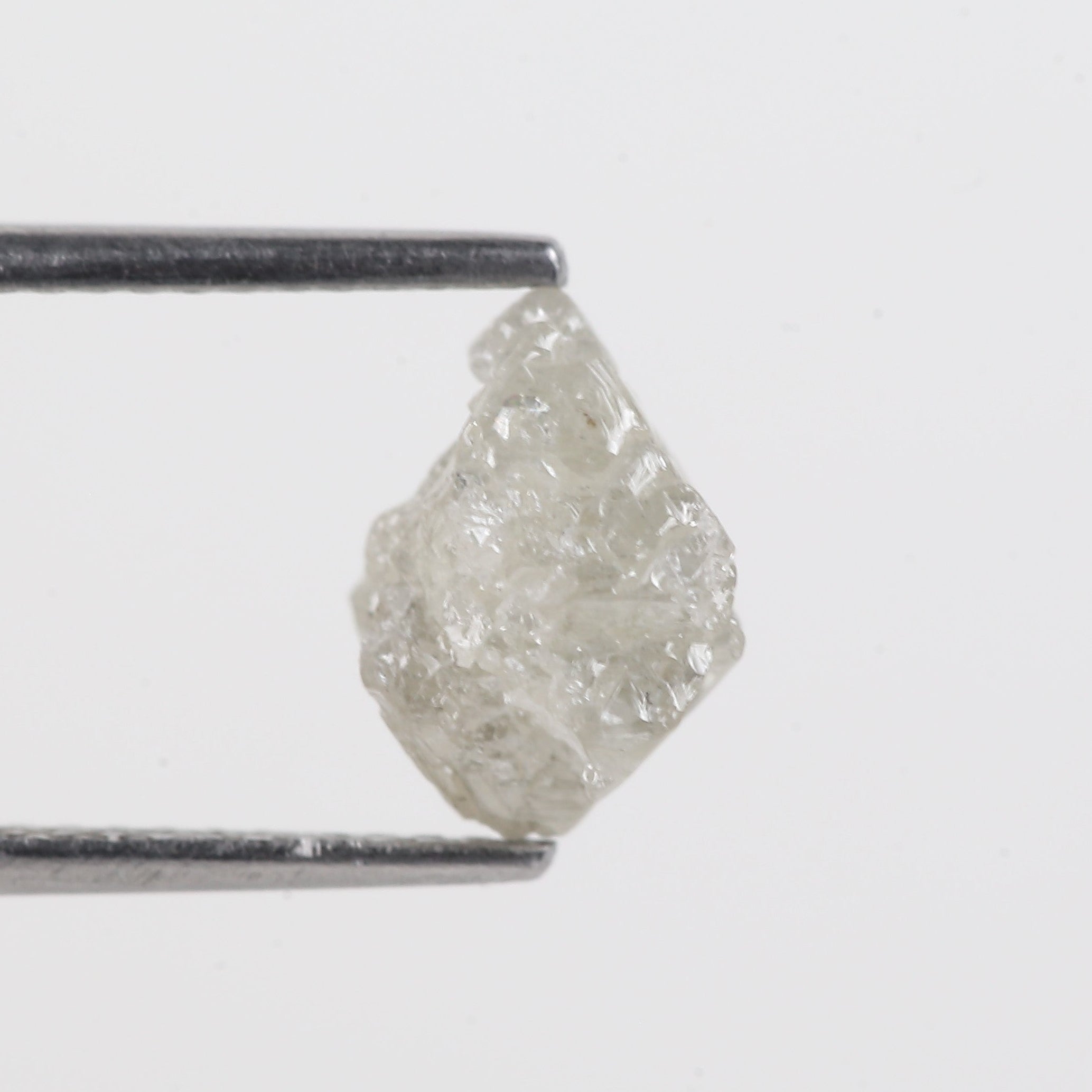 Raw diamond held between tweezers on a white background