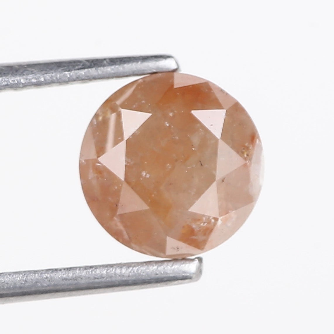 Faceted orange gemstone held by tweezers on a white background