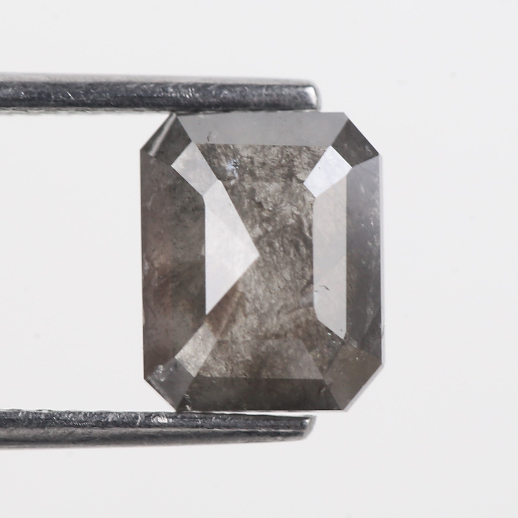 Faceted gemstone held by tweezers on a light gray background
