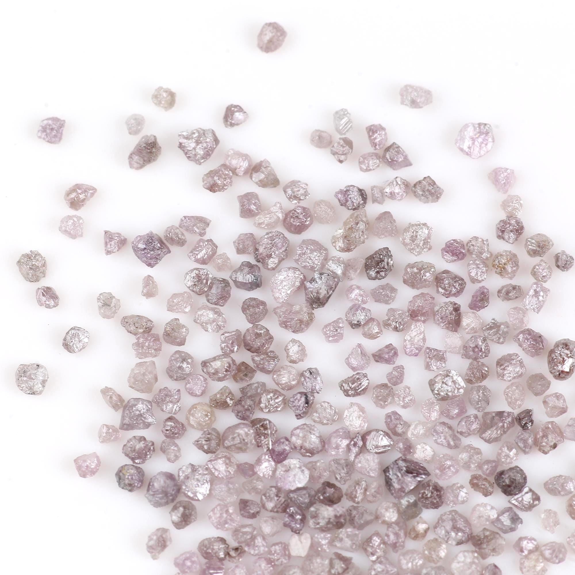 Raw diamonds with pink and gray hues scattered on a white background