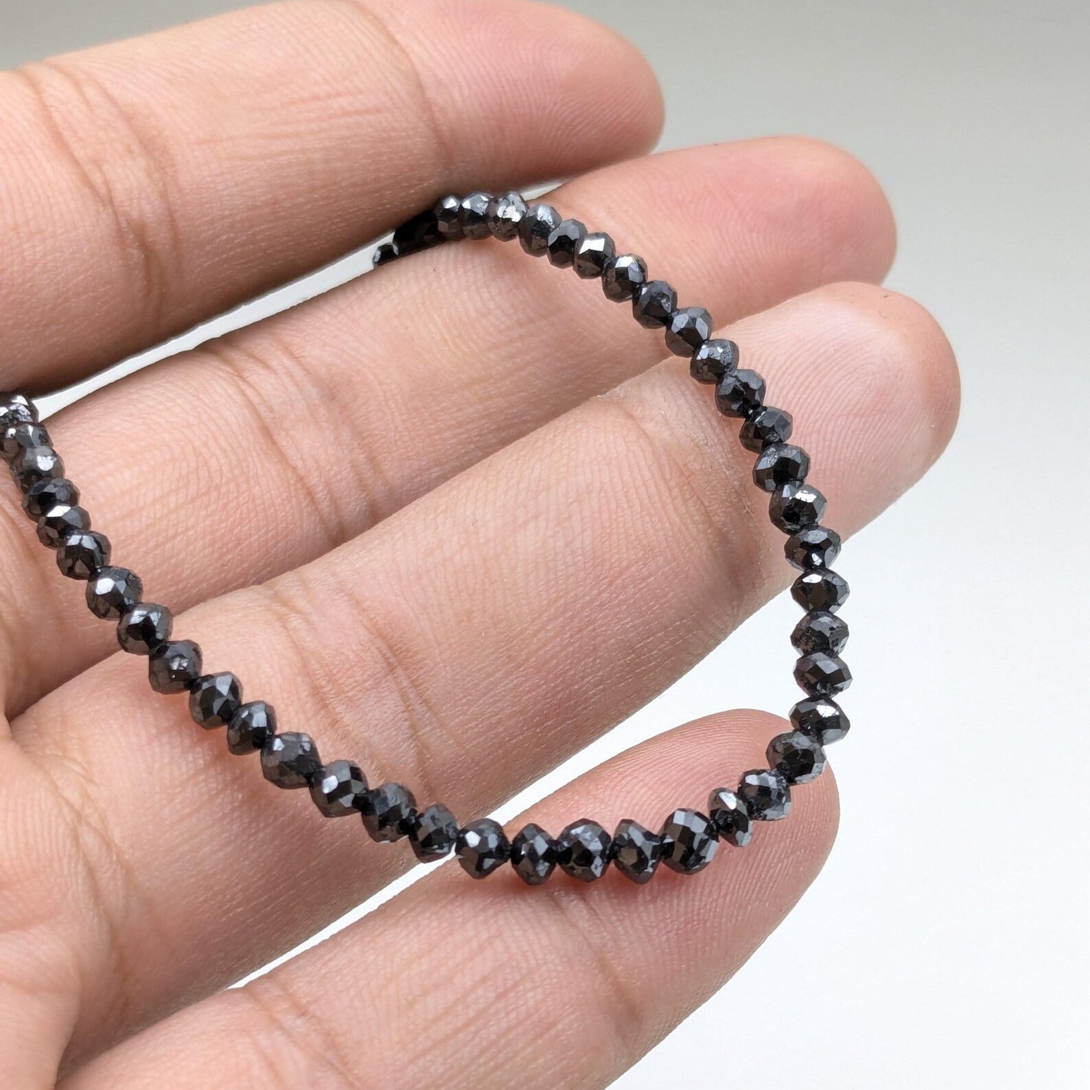 Black beaded bracelet held in a hand against a neutral background