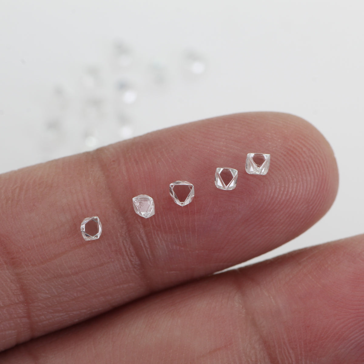 Five small clear faceted diamond displayed on a person's fingertip against a white background.