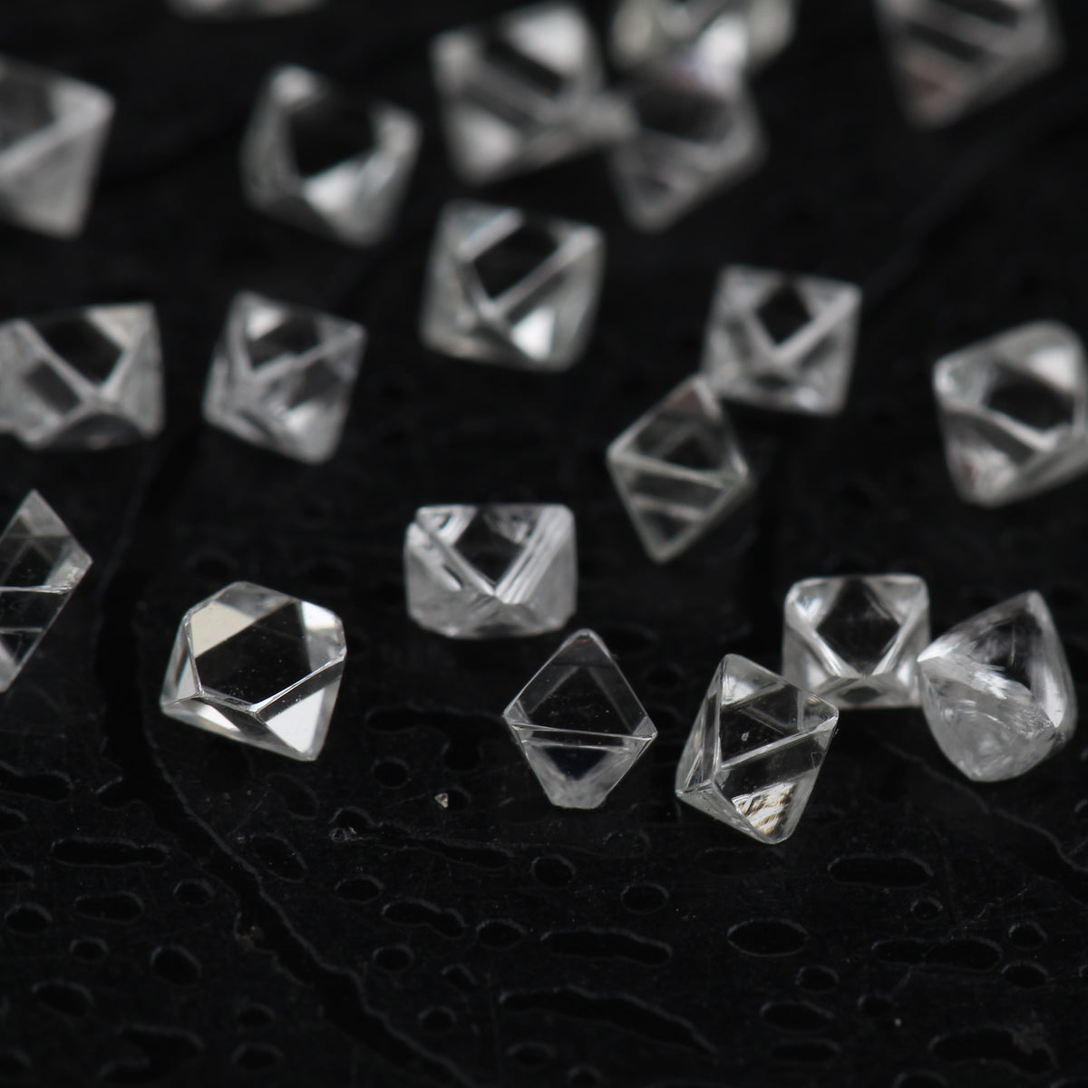 Clear faceted crystal octahedron scattered on a black textured fabric background.
