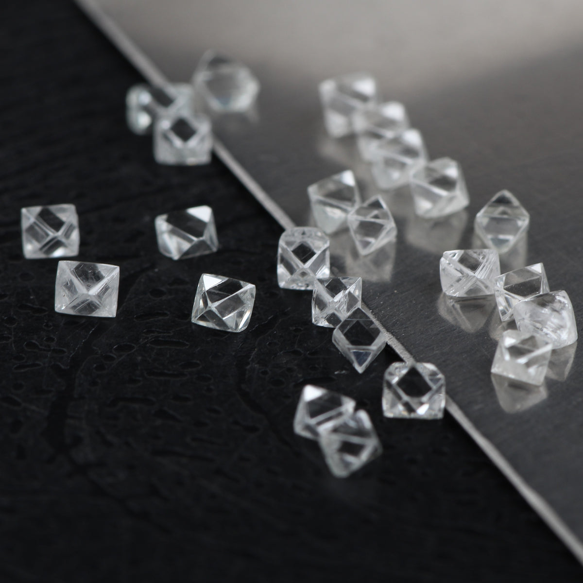 Clear faceted square diamond rough scattered on a glossy black surface.