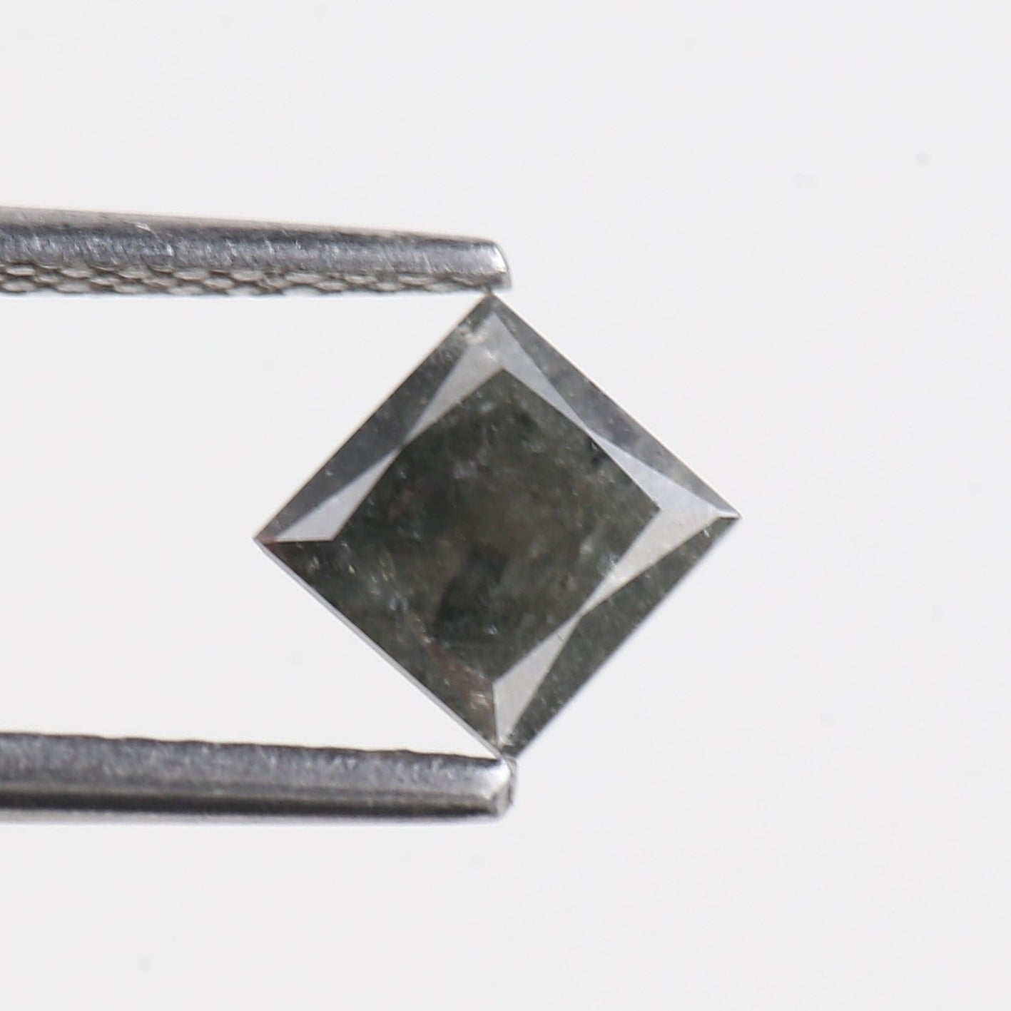 Faceted gemstone held by tweezers on a light gray background