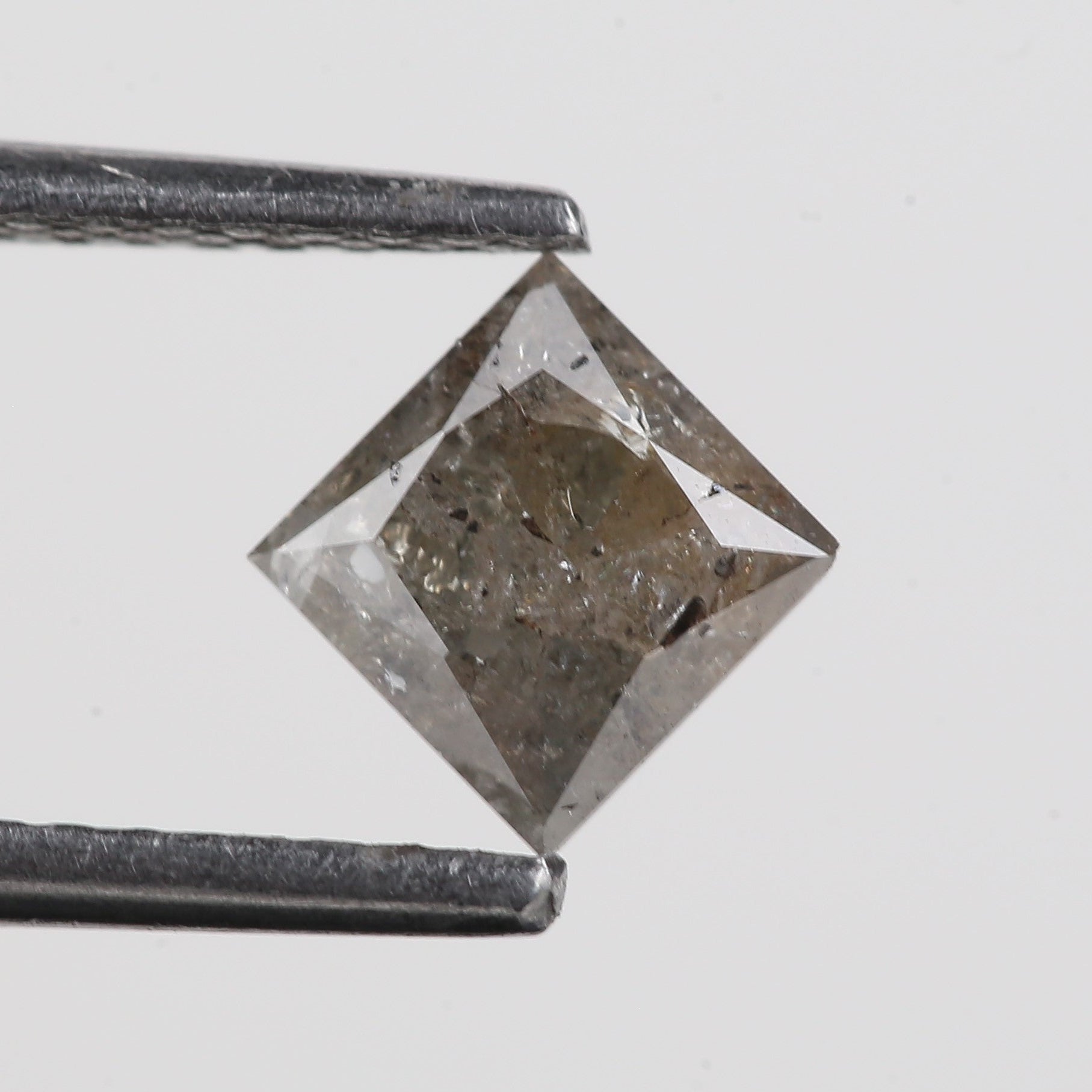 Raw diamond held between tweezers on a light gray background