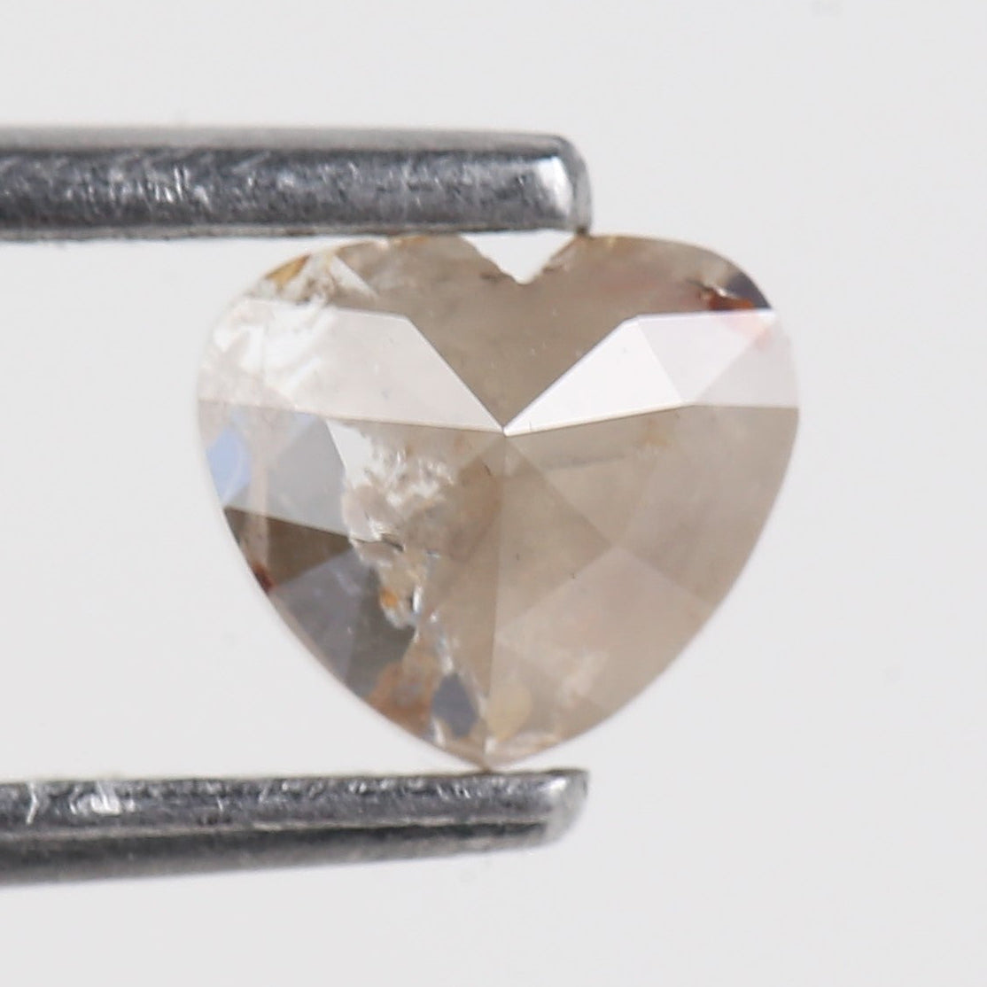 Heart-shaped diamond held between tweezers on a white background