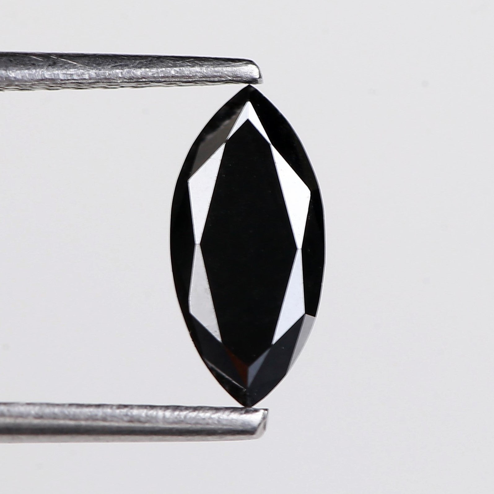 Faceted black gemstone held between tweezers on a light gray background