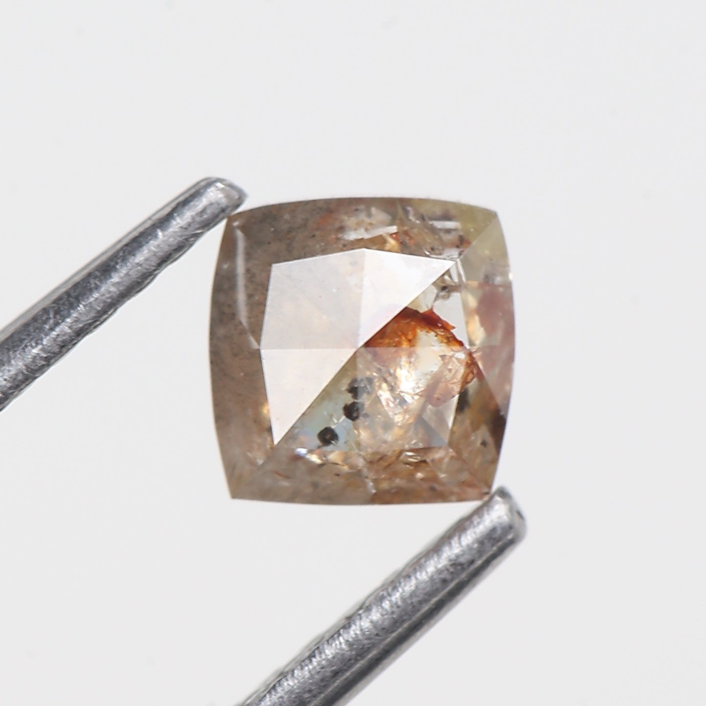 Square-cut diamond held by tweezers on a light gray background
