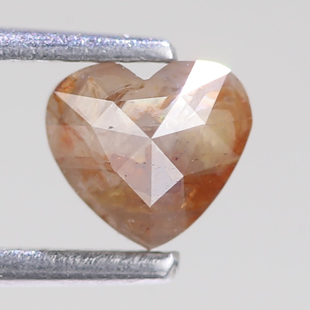 Heart-shaped brownish-orange diamond with a silver ruler for scale on a light gray background