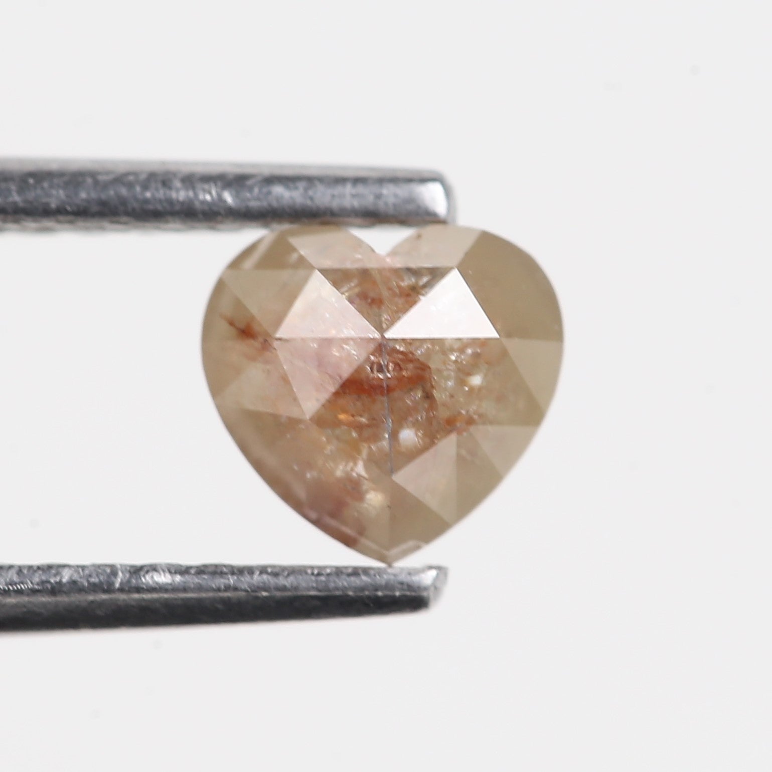 Heart-shaped diamond held by tweezers on a white background