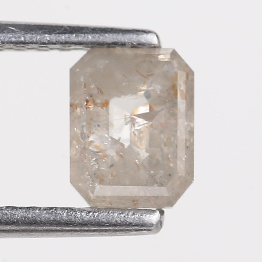 emerald diamond held between two metal prongs on a light gray background