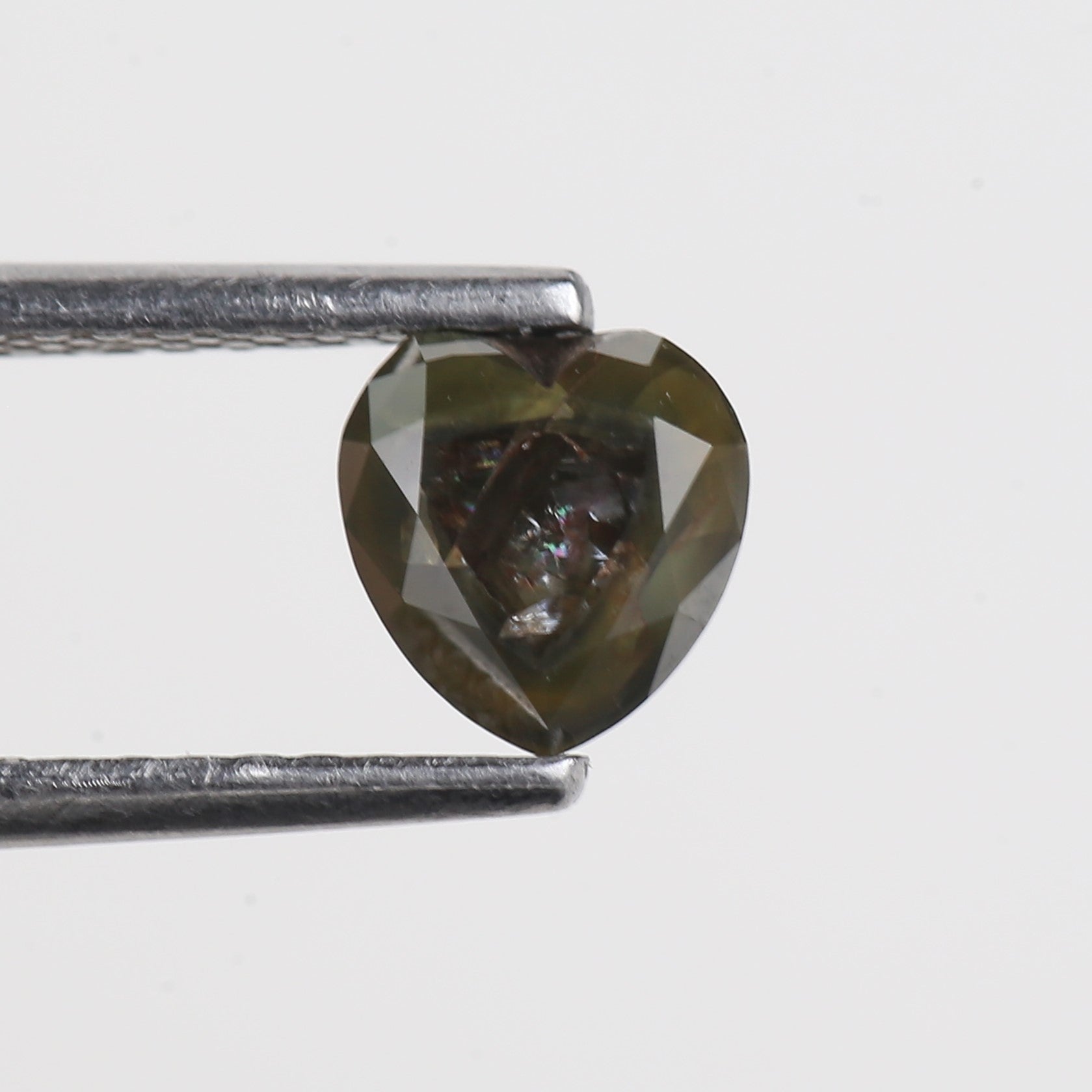 Heart-shaped diamond held between tweezers on a light gray background
