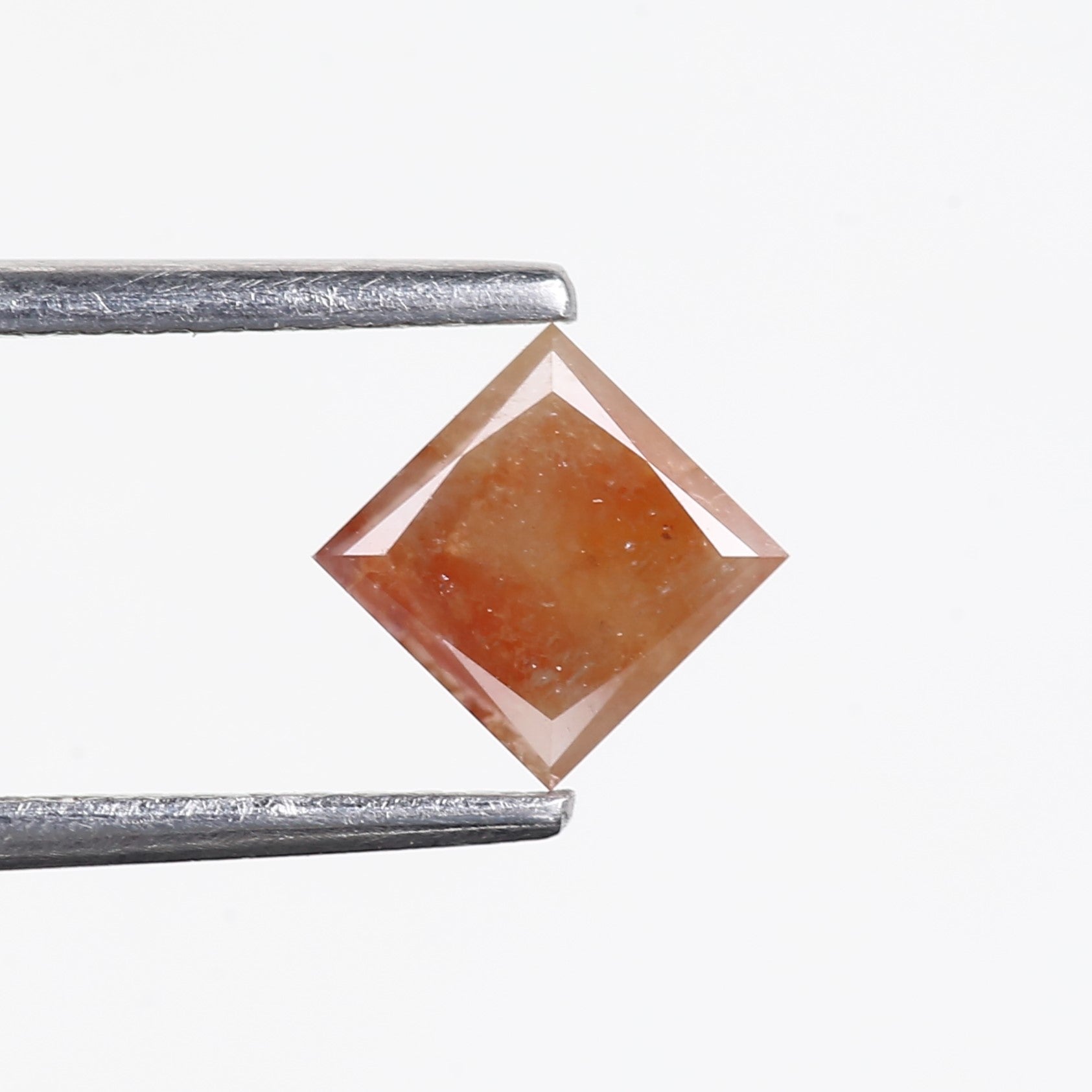 Square-cut gemstone held between tweezers on a white background
