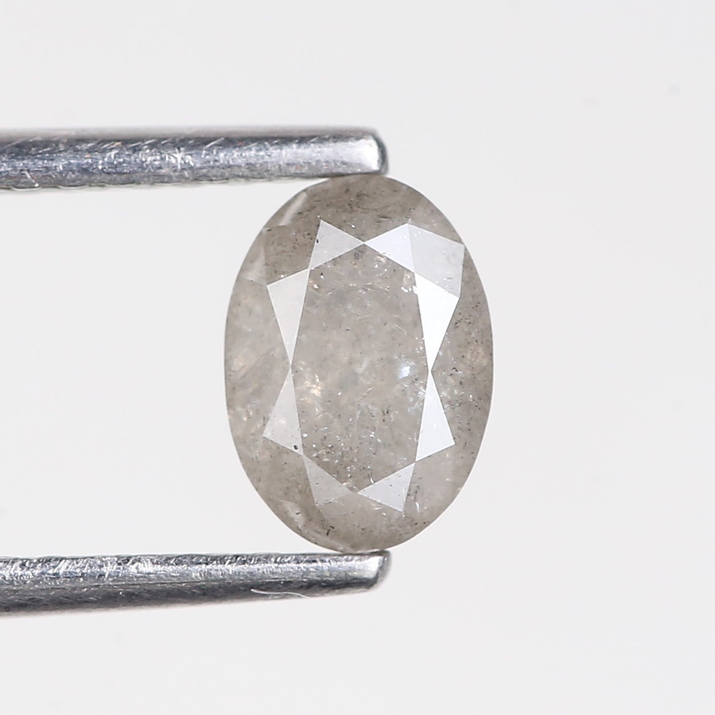 Oval-shaped diamond held between two tweezers on a light gray background