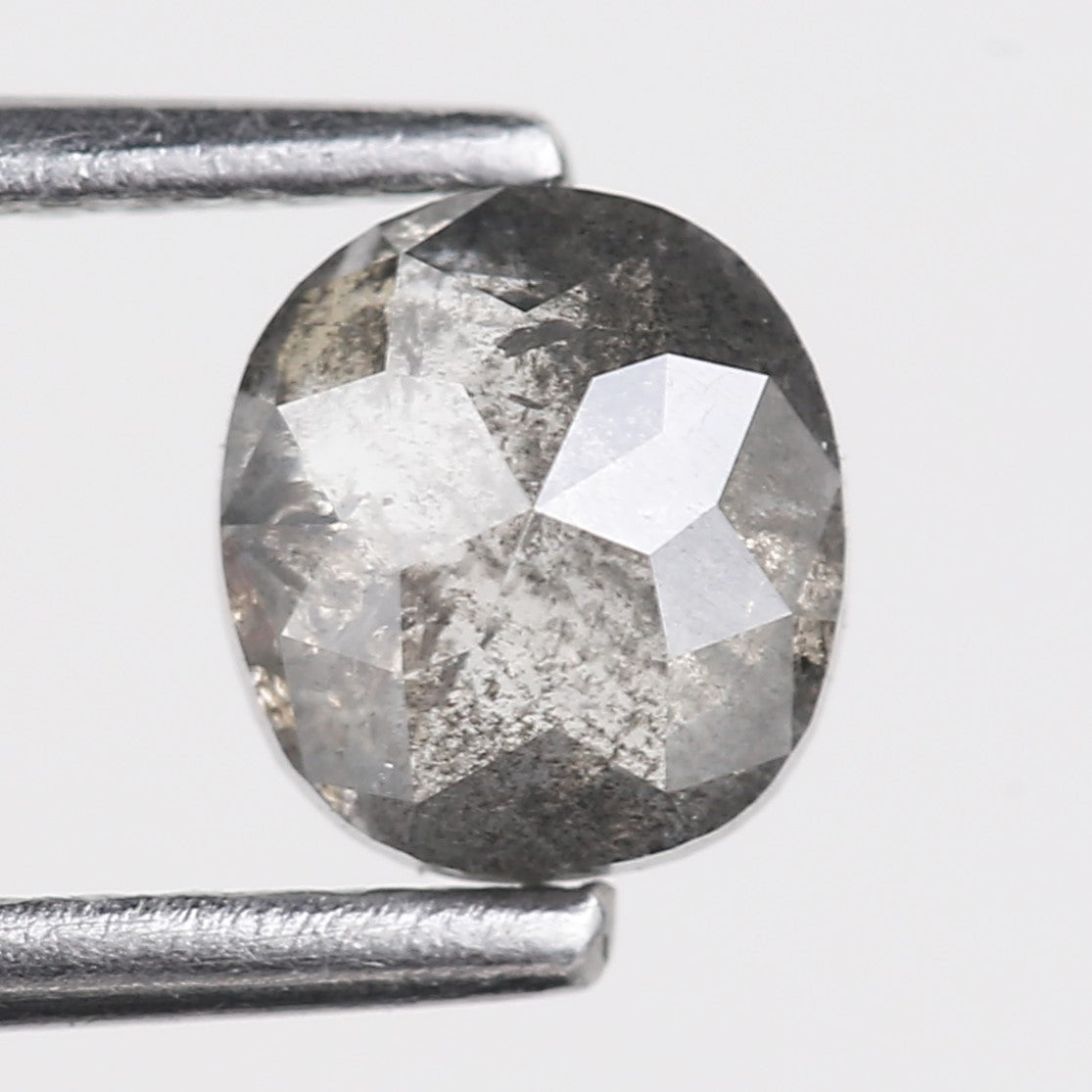 oval cut diamond with grayish color held between two metal prongs on a light gray background