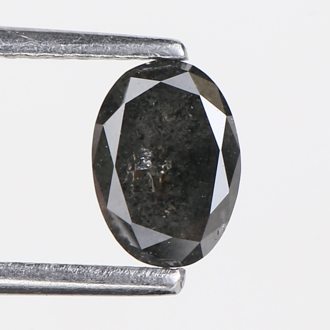 Faceted black gemstone held between two metal prongs on a light gray background