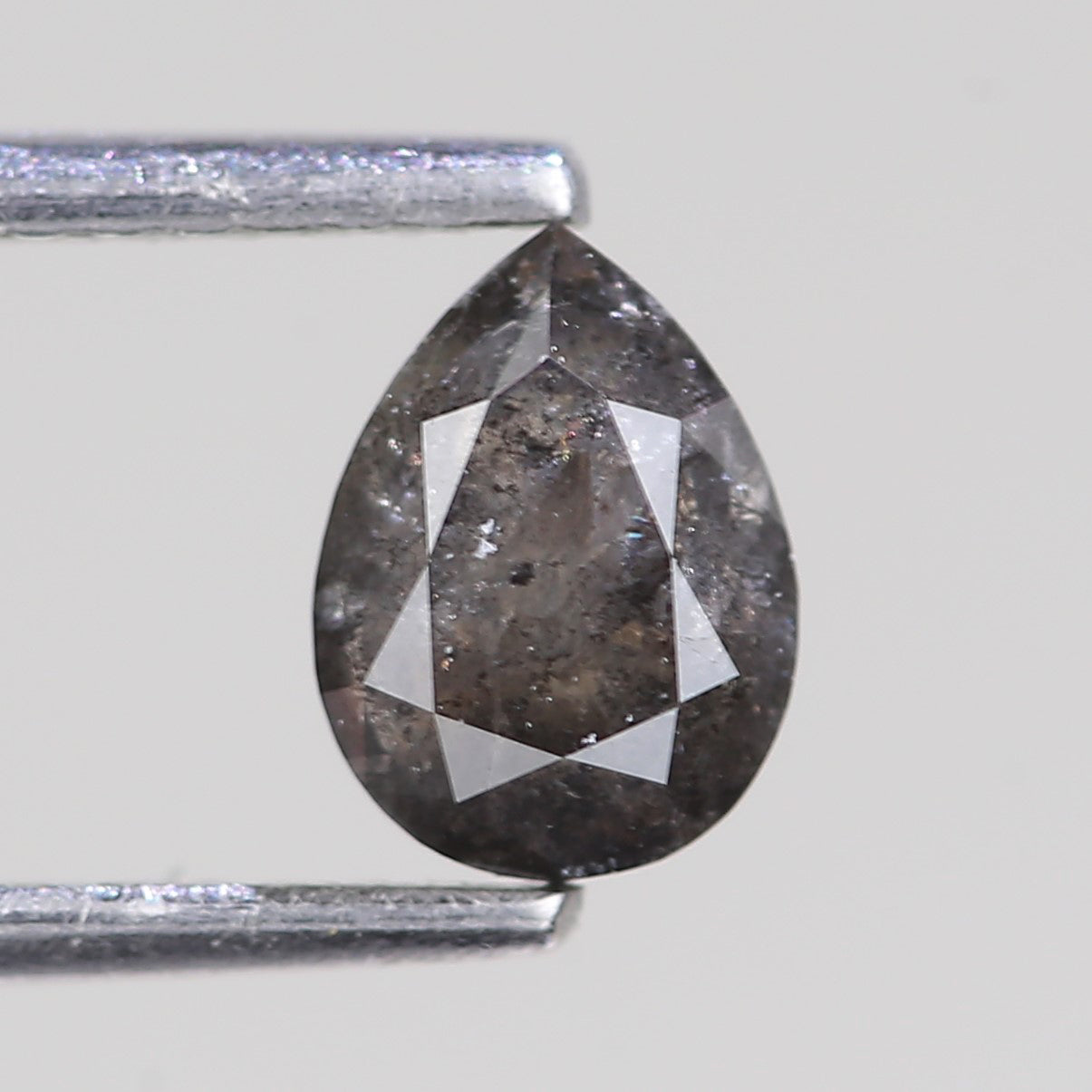 Teardrop-shaped diamond held between two metal prongs on a light gray background