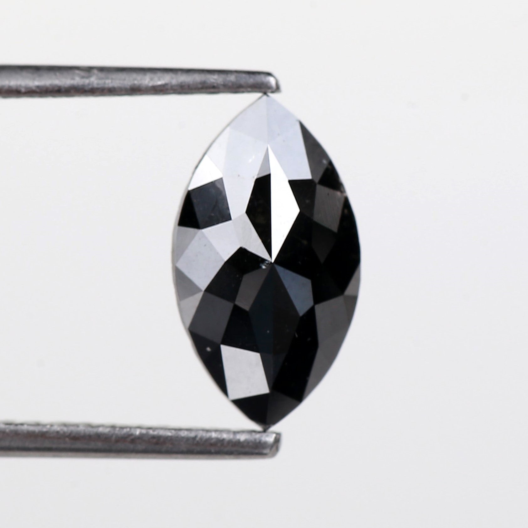 Faceted black diamond held between tweezers on a white background
