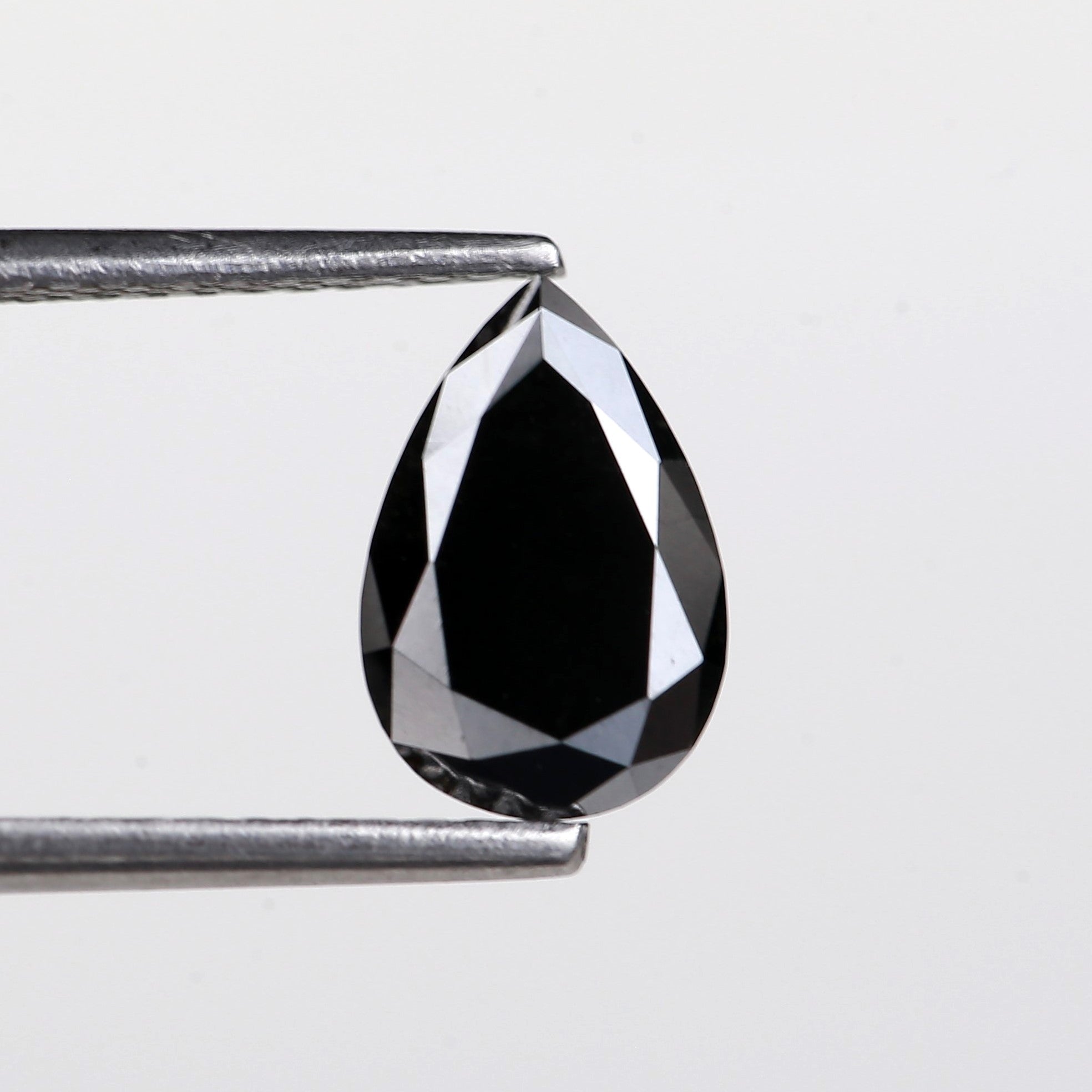 Teardrop-shaped black diamond held between two silver prongs against a light gray background