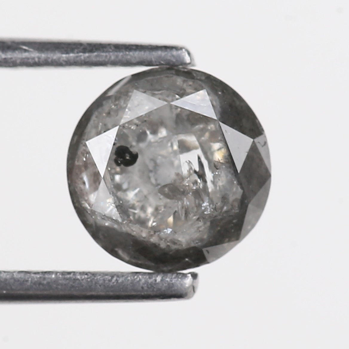 Faceted gemstone held between tweezers on a light gray background