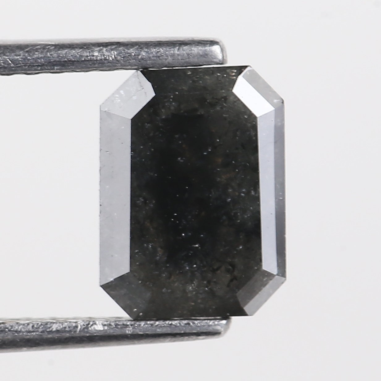 Faceted black gemstone held by tweezers on a light gray background