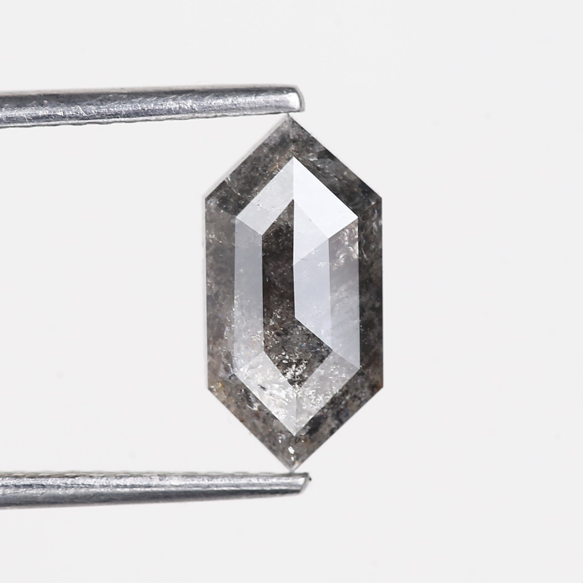 Hexagonal diamond held by tweezers on a light gray background