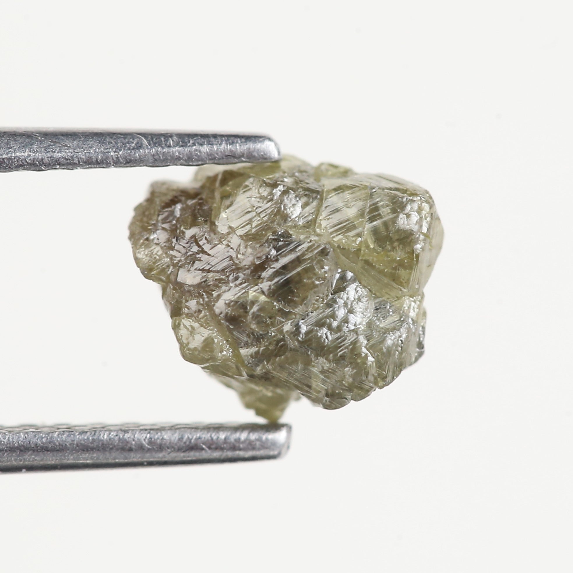 Raw diamond held between two metal prongs on a white background