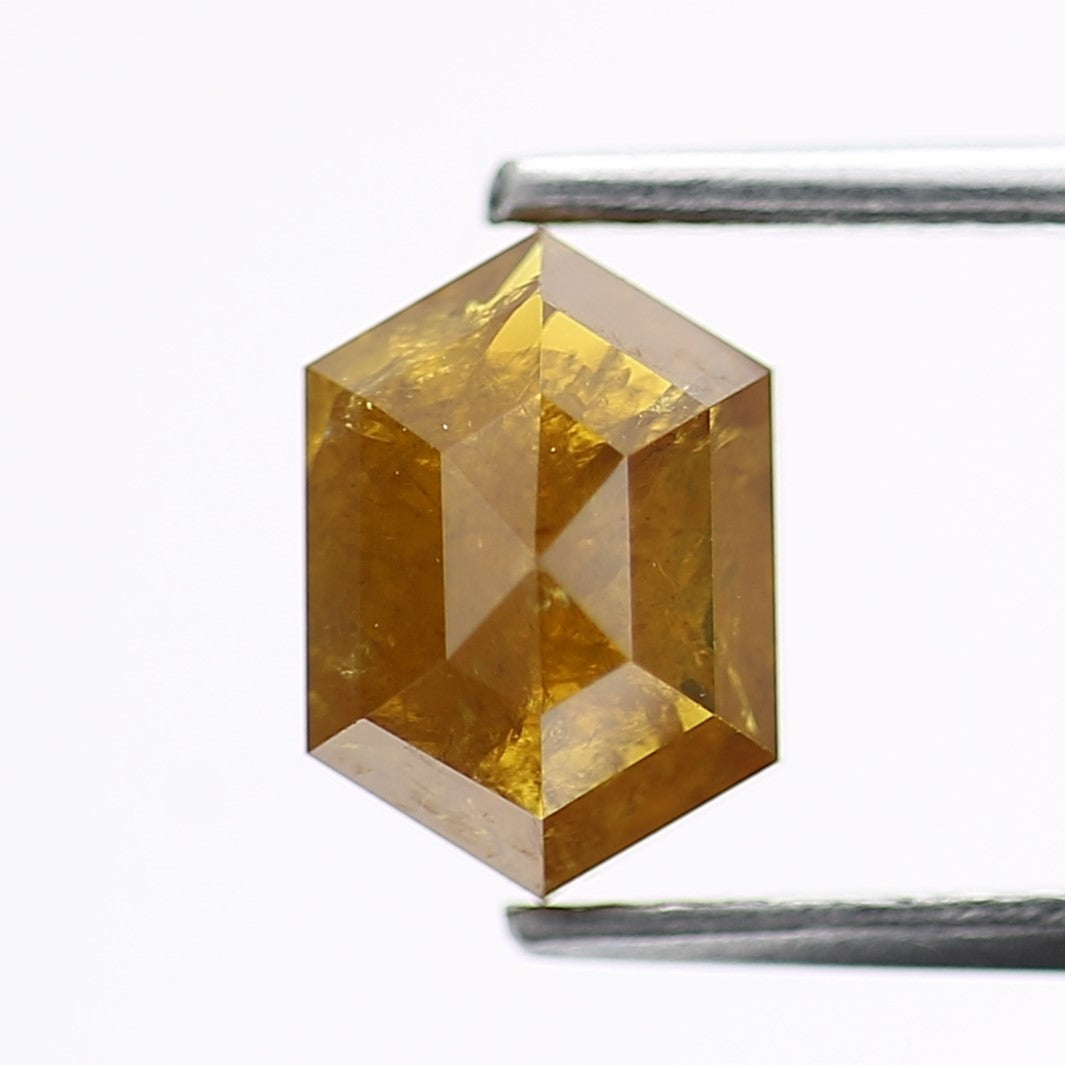 Faceted yellow gemstone with a metal rod for scale on a white background