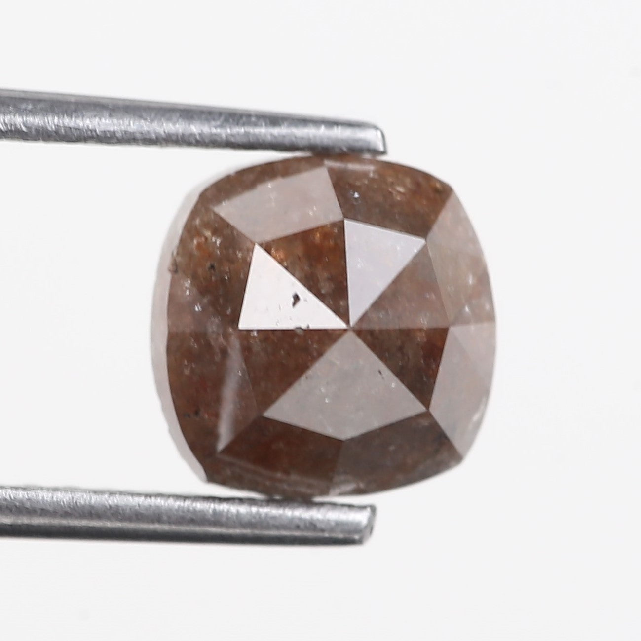 Brown diamond held between two metal prongs on a white background