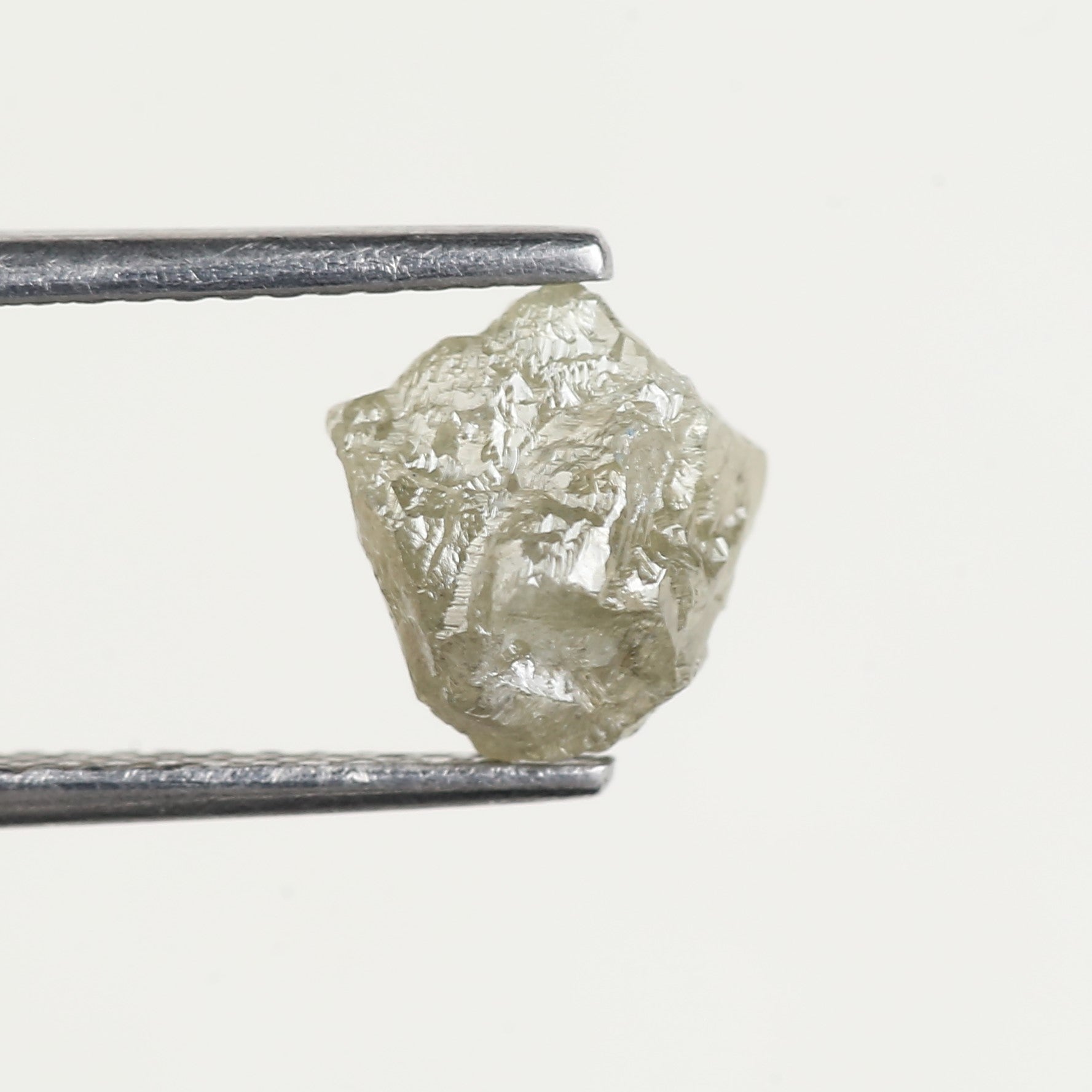 Raw diamond held by tweezers on a white background