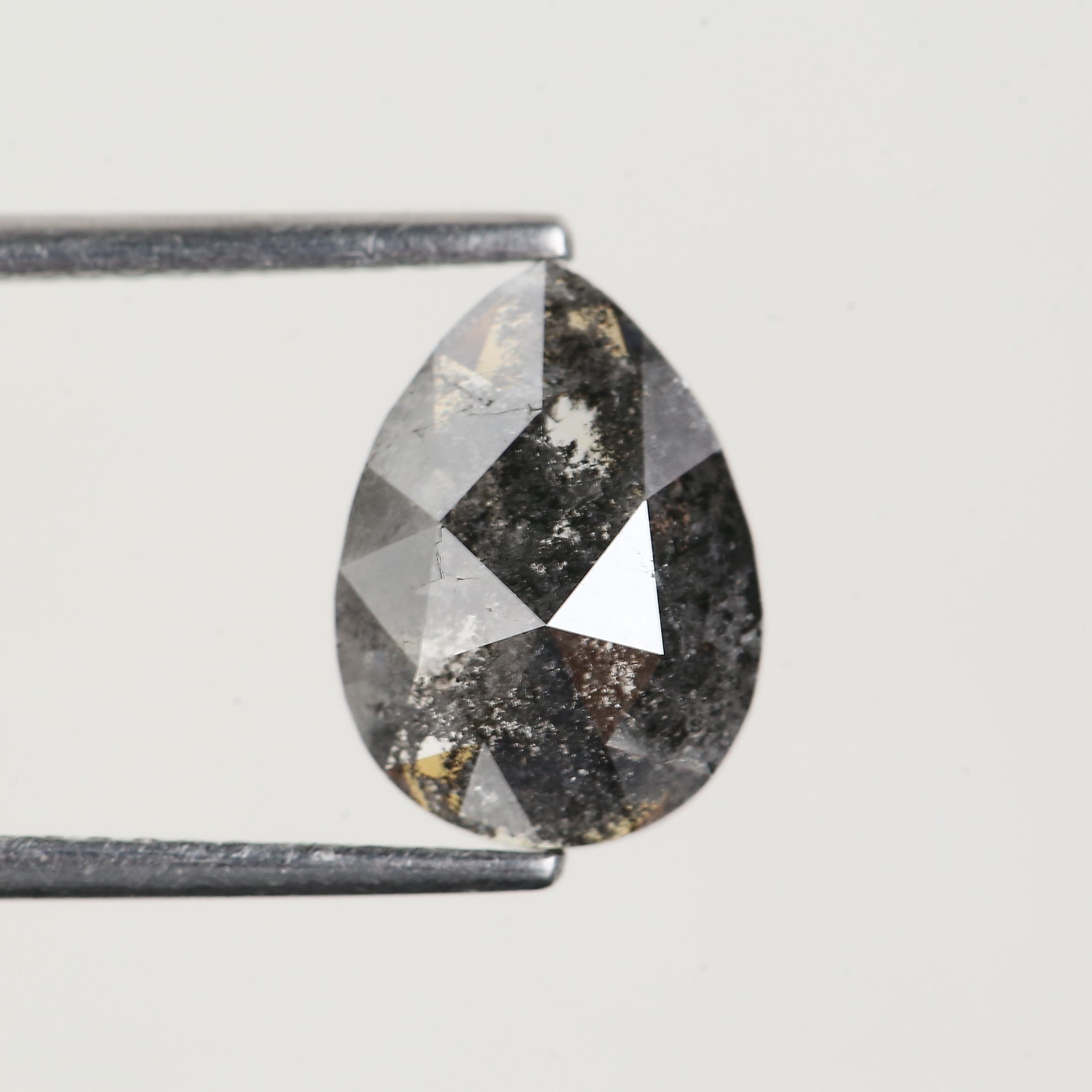 Teardrop-shaped diamond held by tweezers on a light gray background