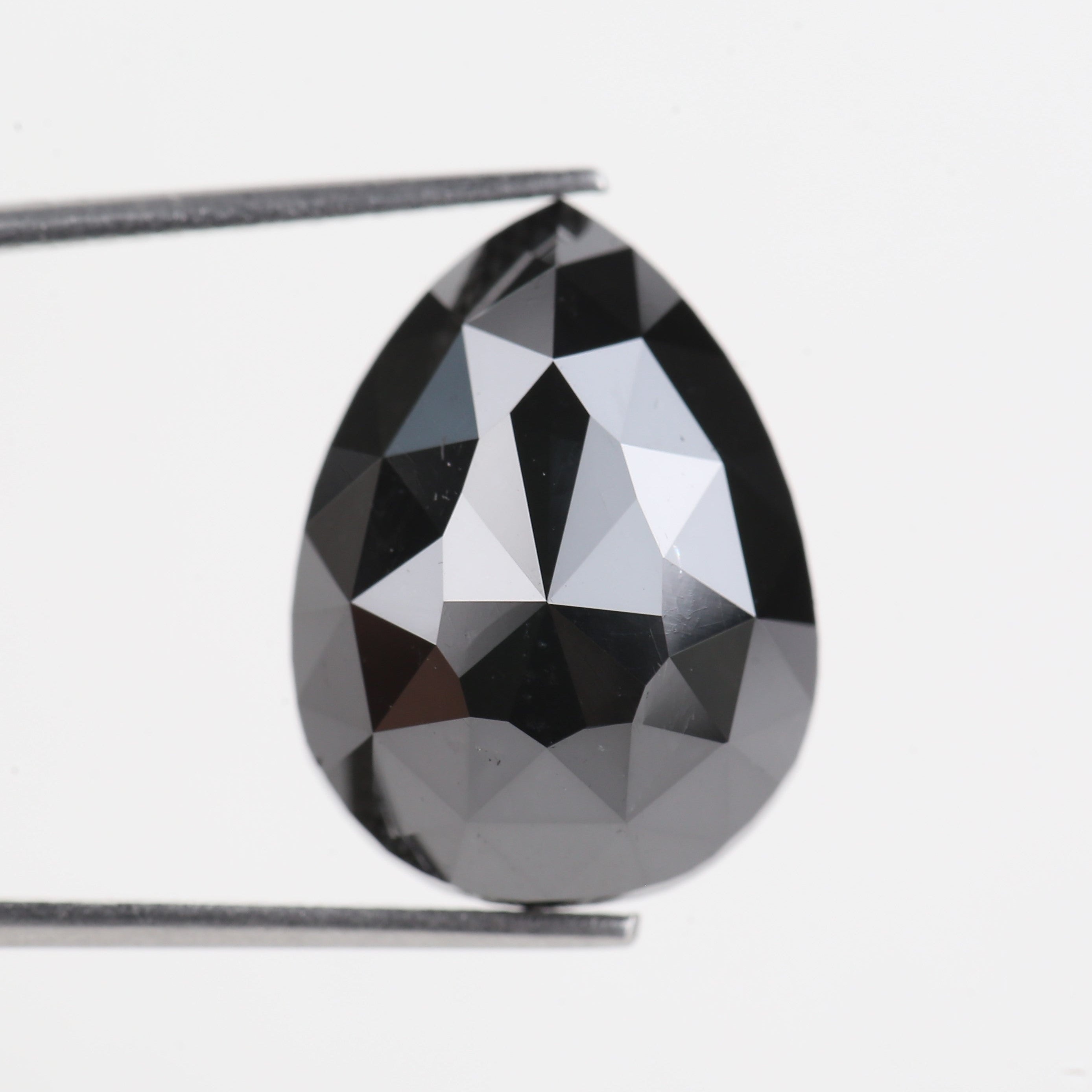 Faceted black gemstone held by tweezers on a white background