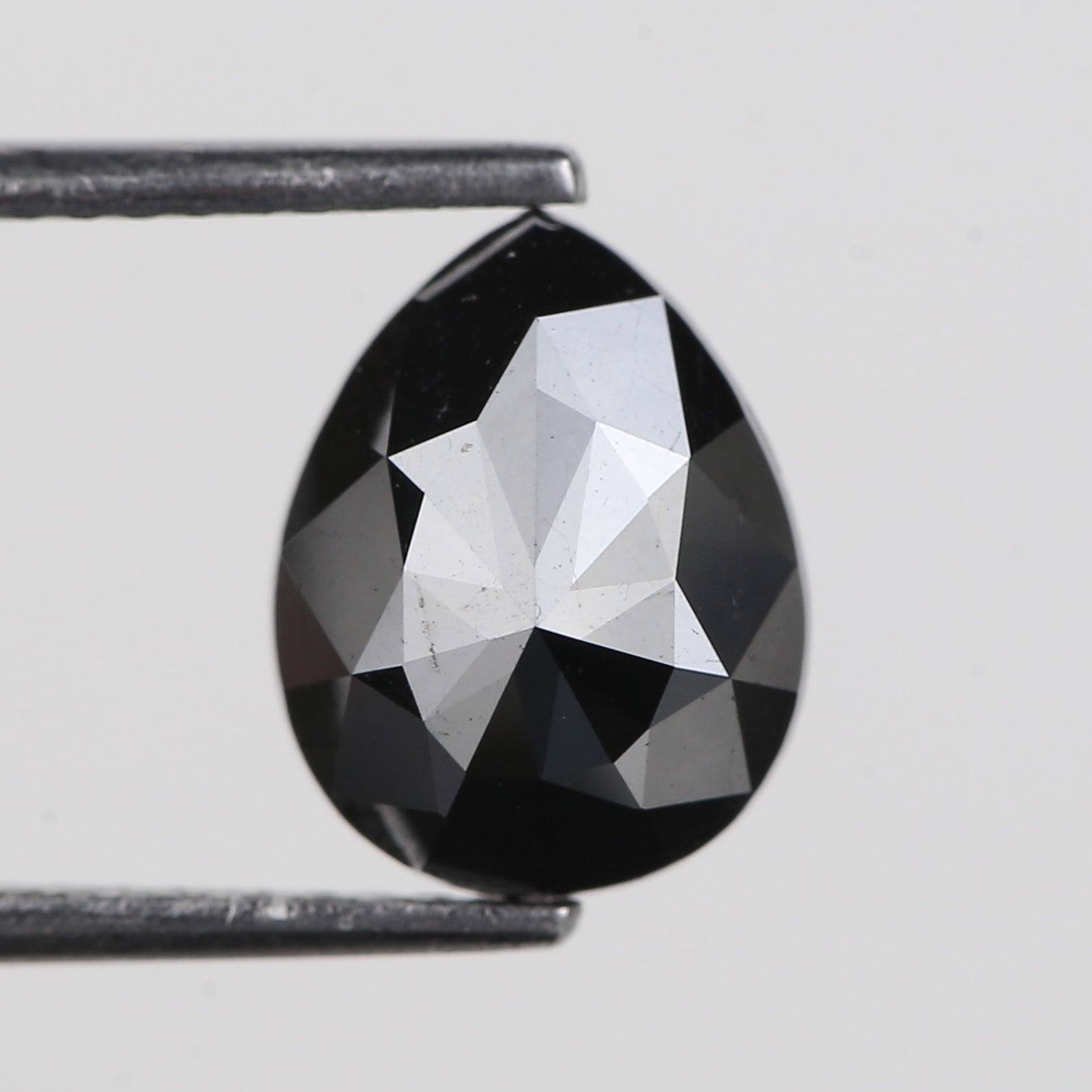 Faceted black pear diamond held between tweezers on a light gray background