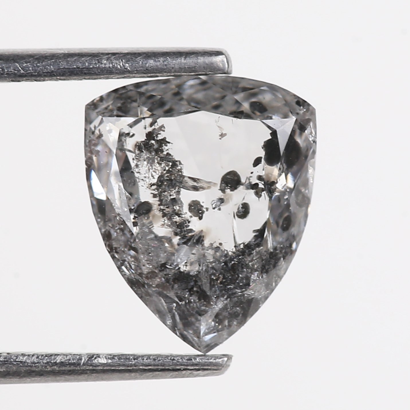 Trillion-shaped diamond with inclusions held by tweezers on a light gray background