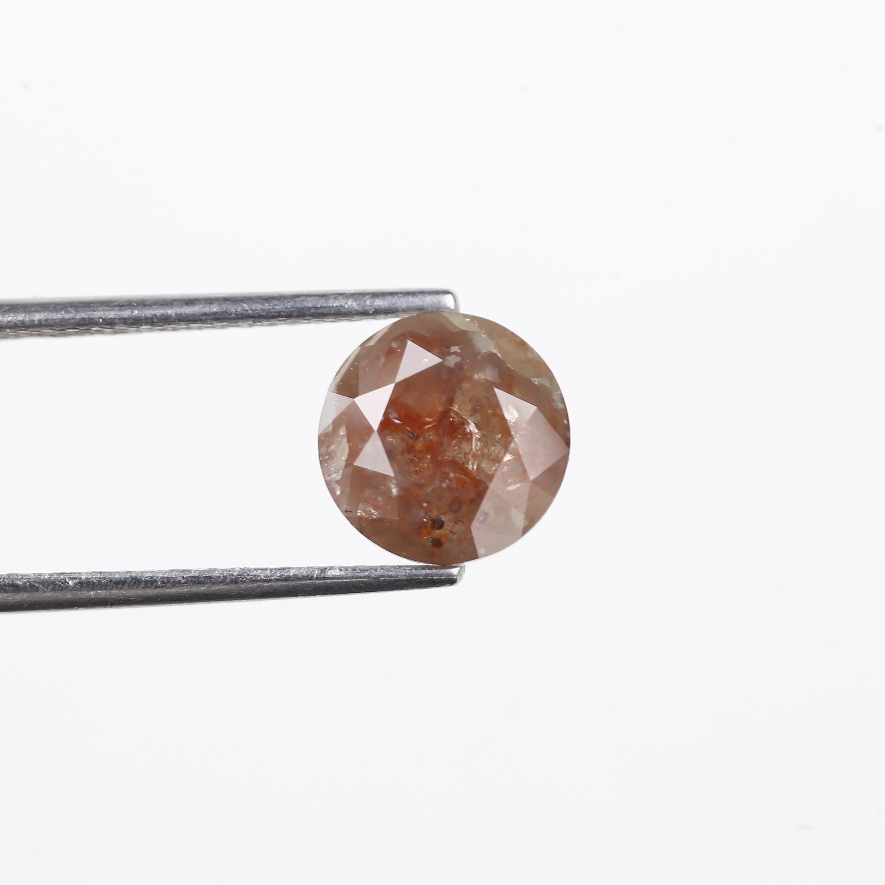 Faceted brown gemstone held by tweezers on a white background