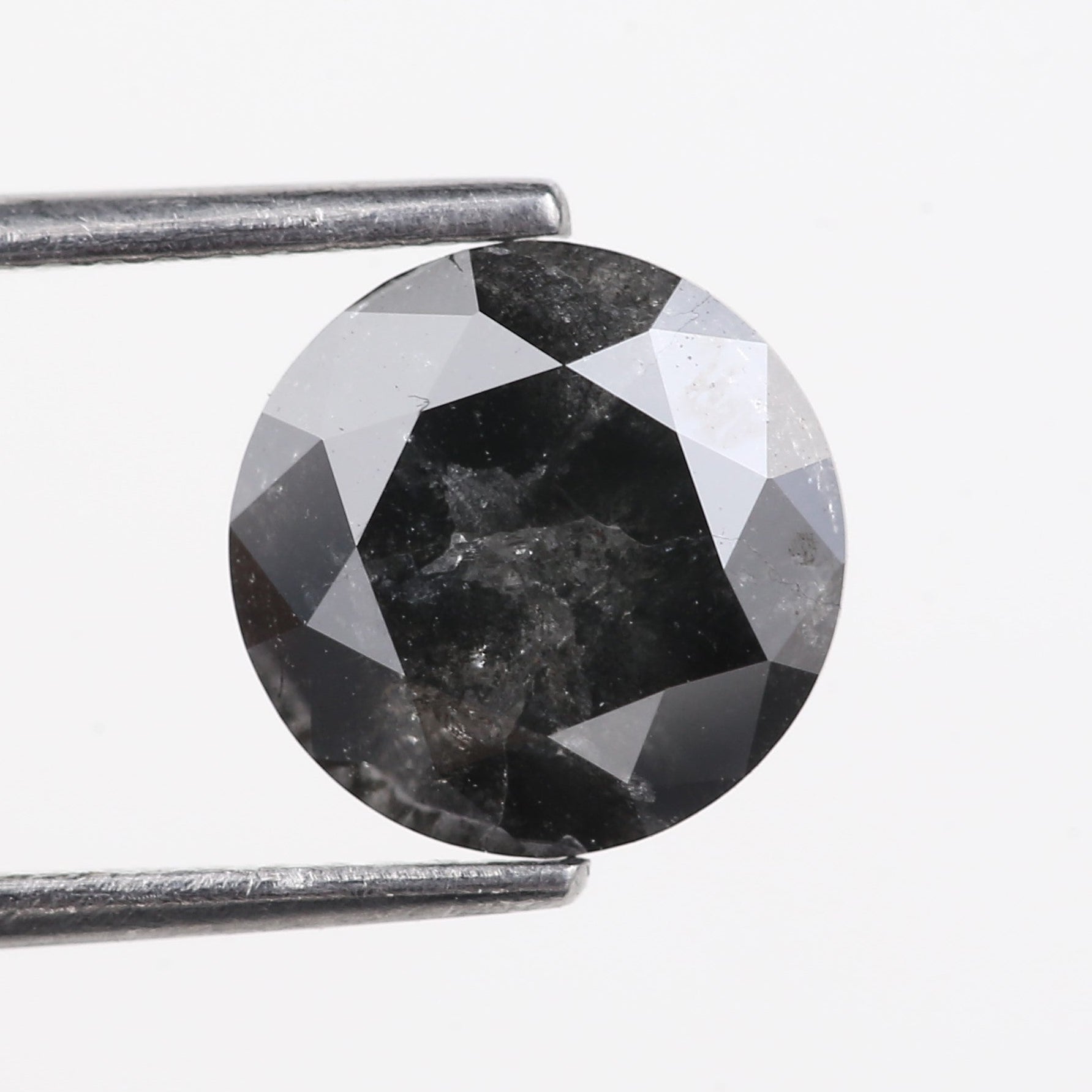 Faceted black gemstone held by tweezers on a white background