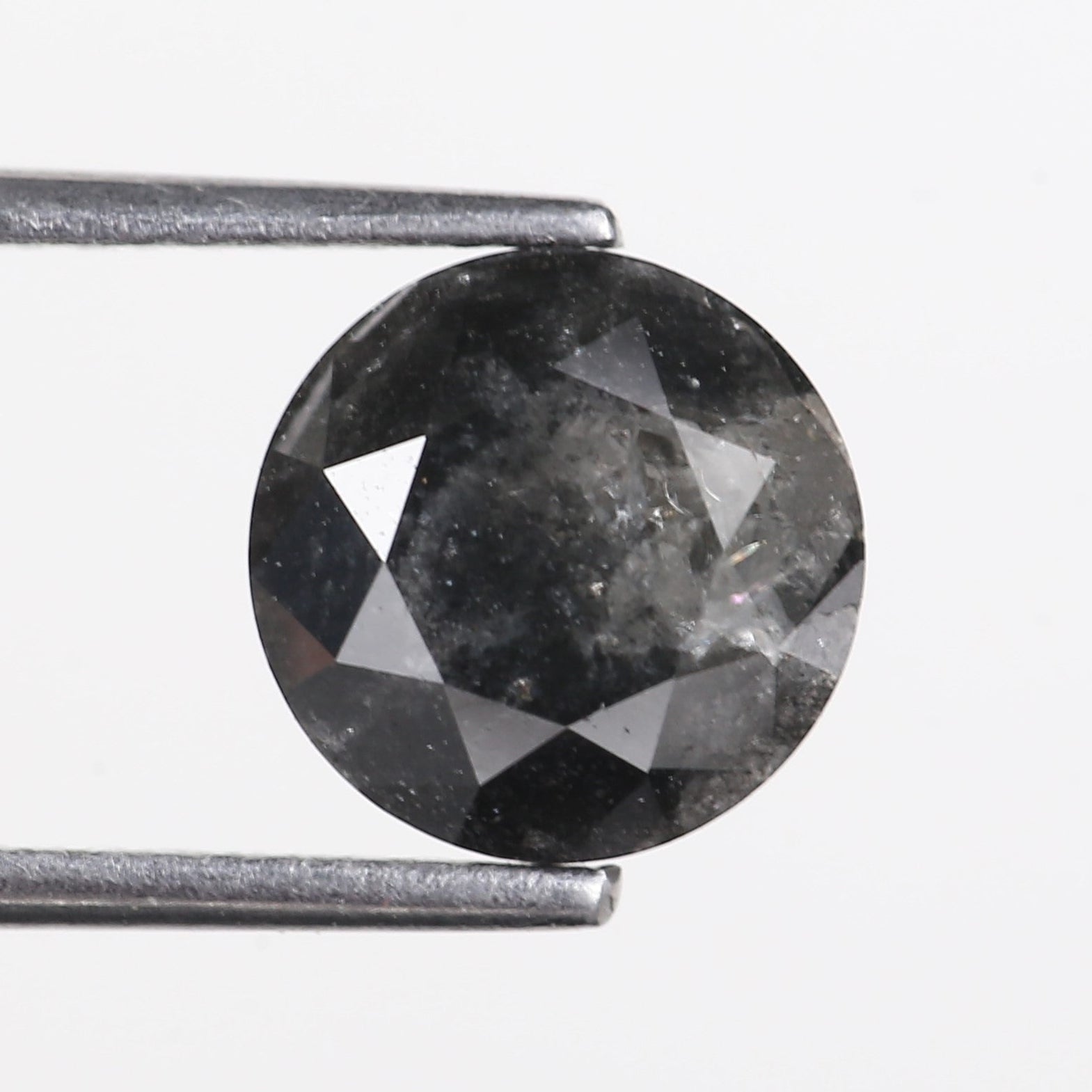 Round black diamond held by tweezers on a light gray background
