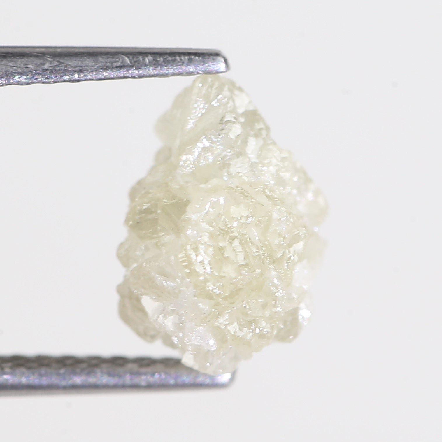 Raw diamond held between tweezers on a white background