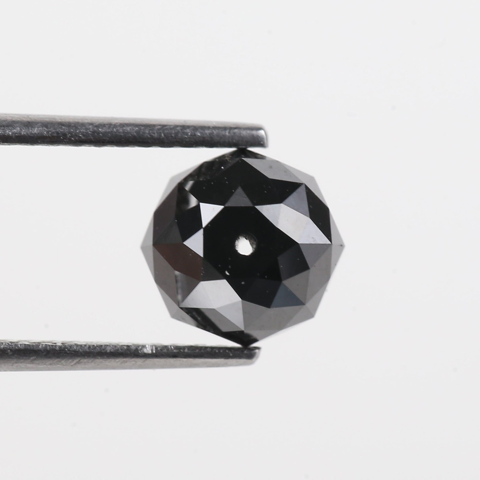 Faceted black gemstone held between tweezers on a light gray background