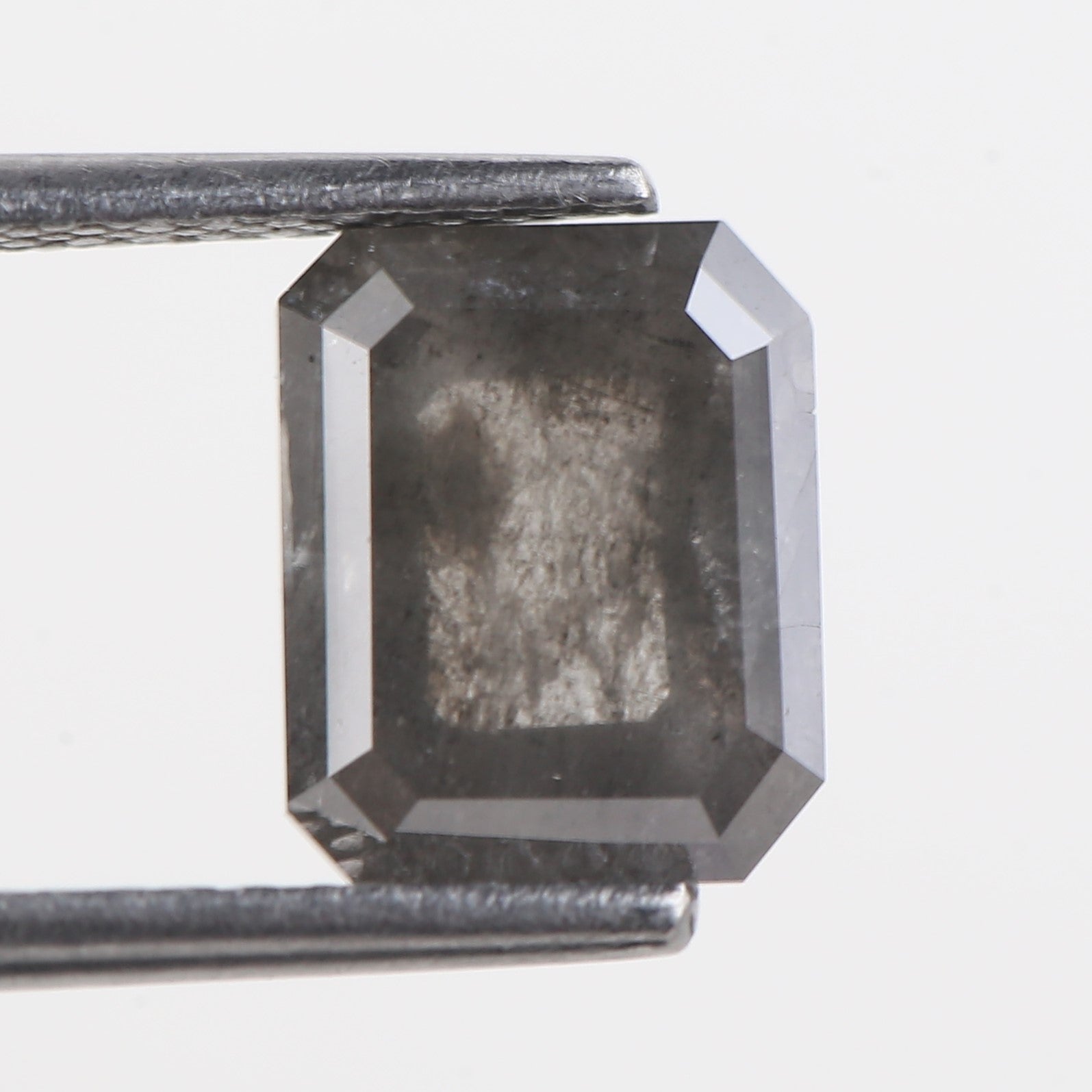 Faceted black diamond held between tweezers on a white background