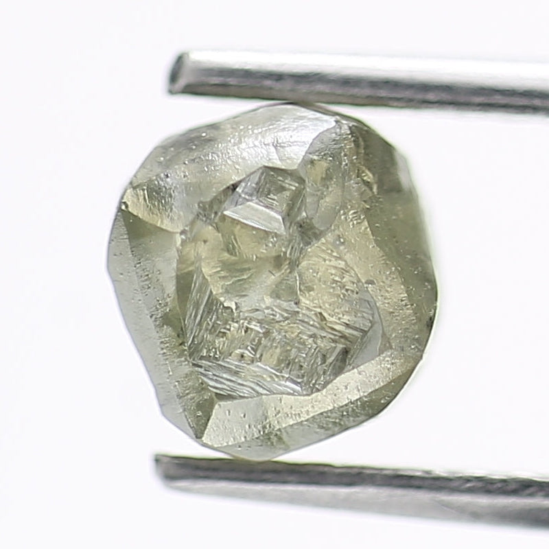 Raw diamond held between tweezers on a white background