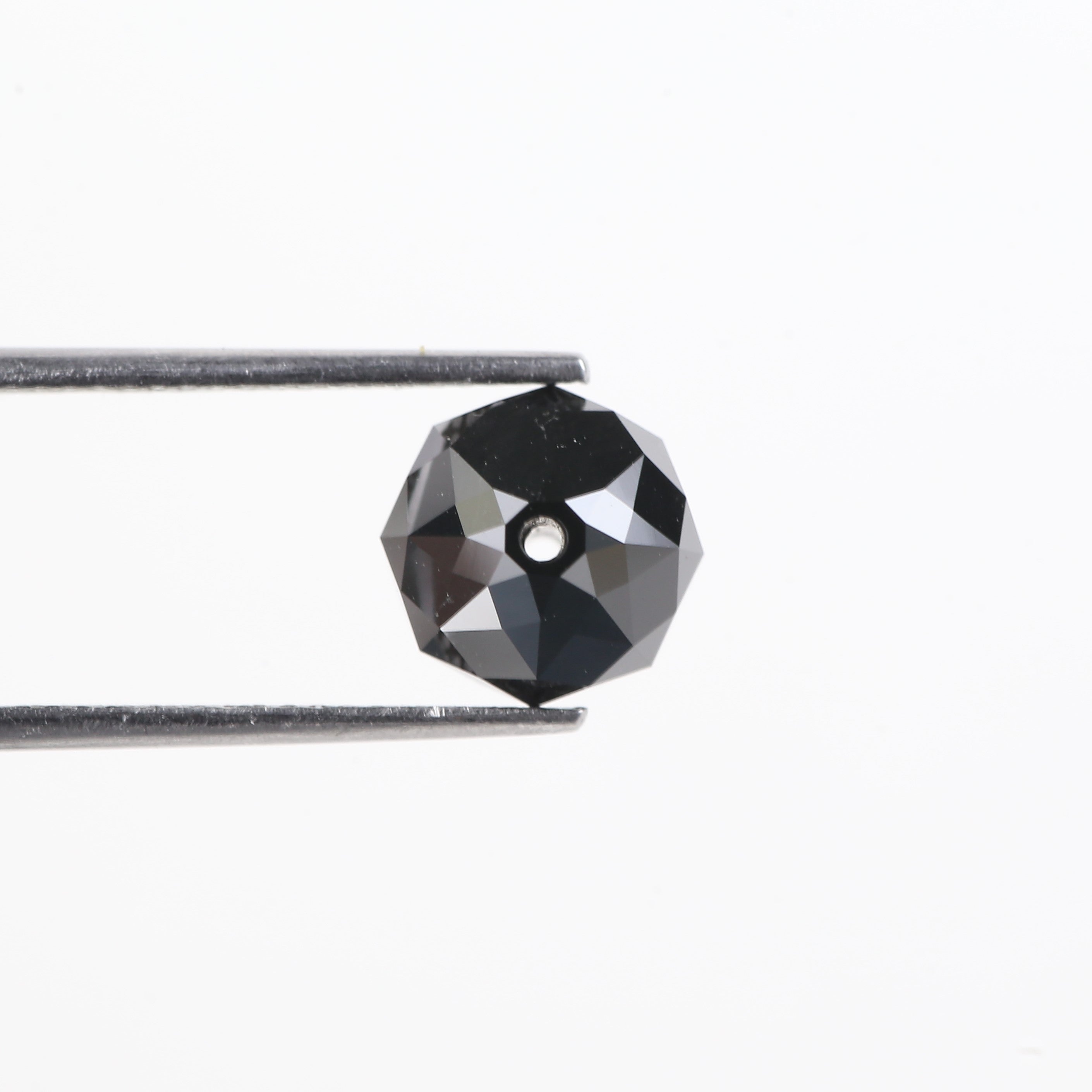 Faceted black gemstone held between tweezers on a white background