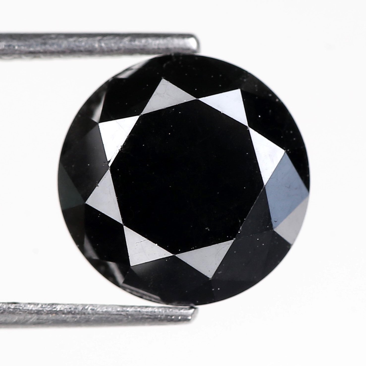 Faceted black DIAMOND held between tweezers on a white background