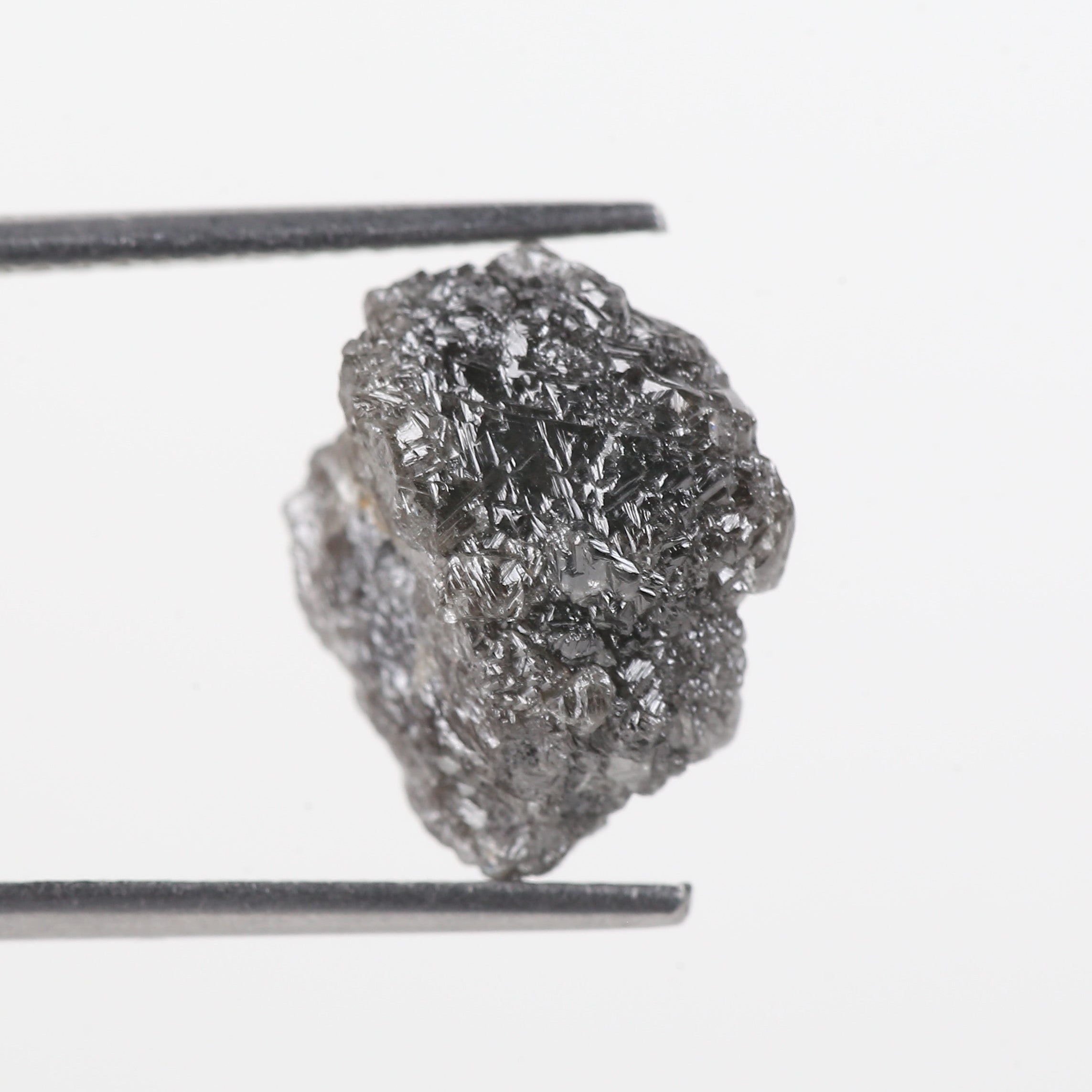 Raw diamond held between tweezers on a white background